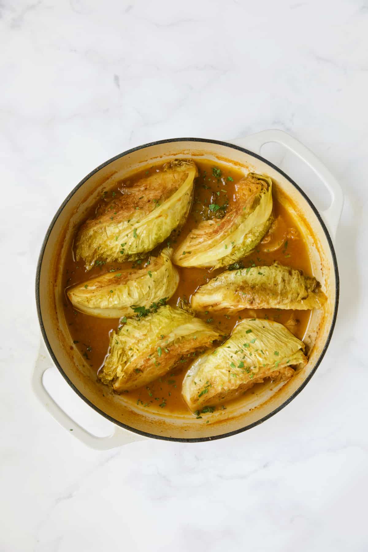 Six cabbage wedges in white enamel cast iron skillet.