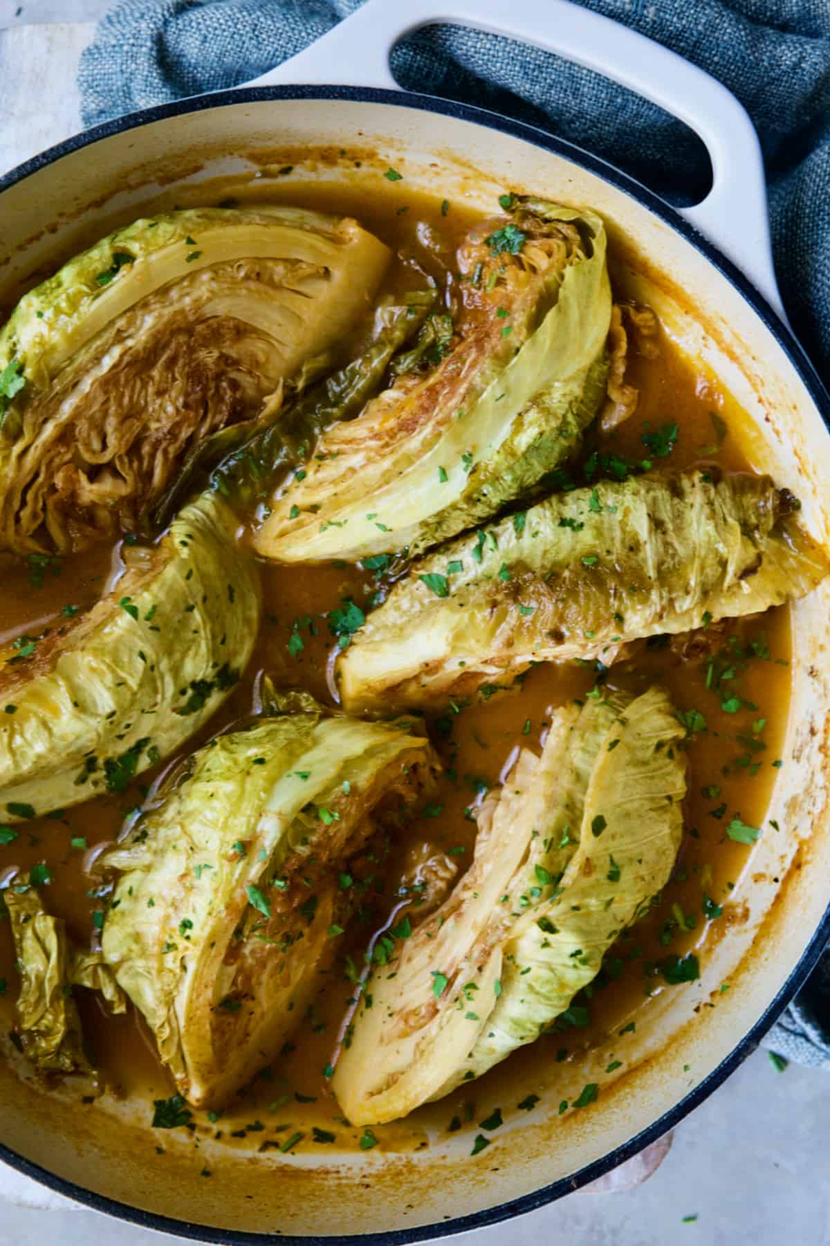 Cider Vinegar Braised Cabbage Wedges in white enamel cast iron skillet garnished with fresh parsley.