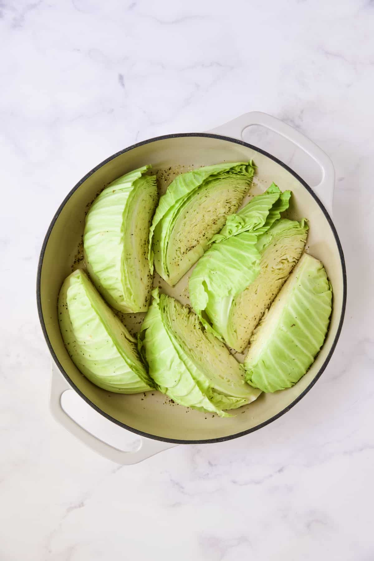 Six cabbage wedges in white enamel cast iron skillet before being browned and braised.