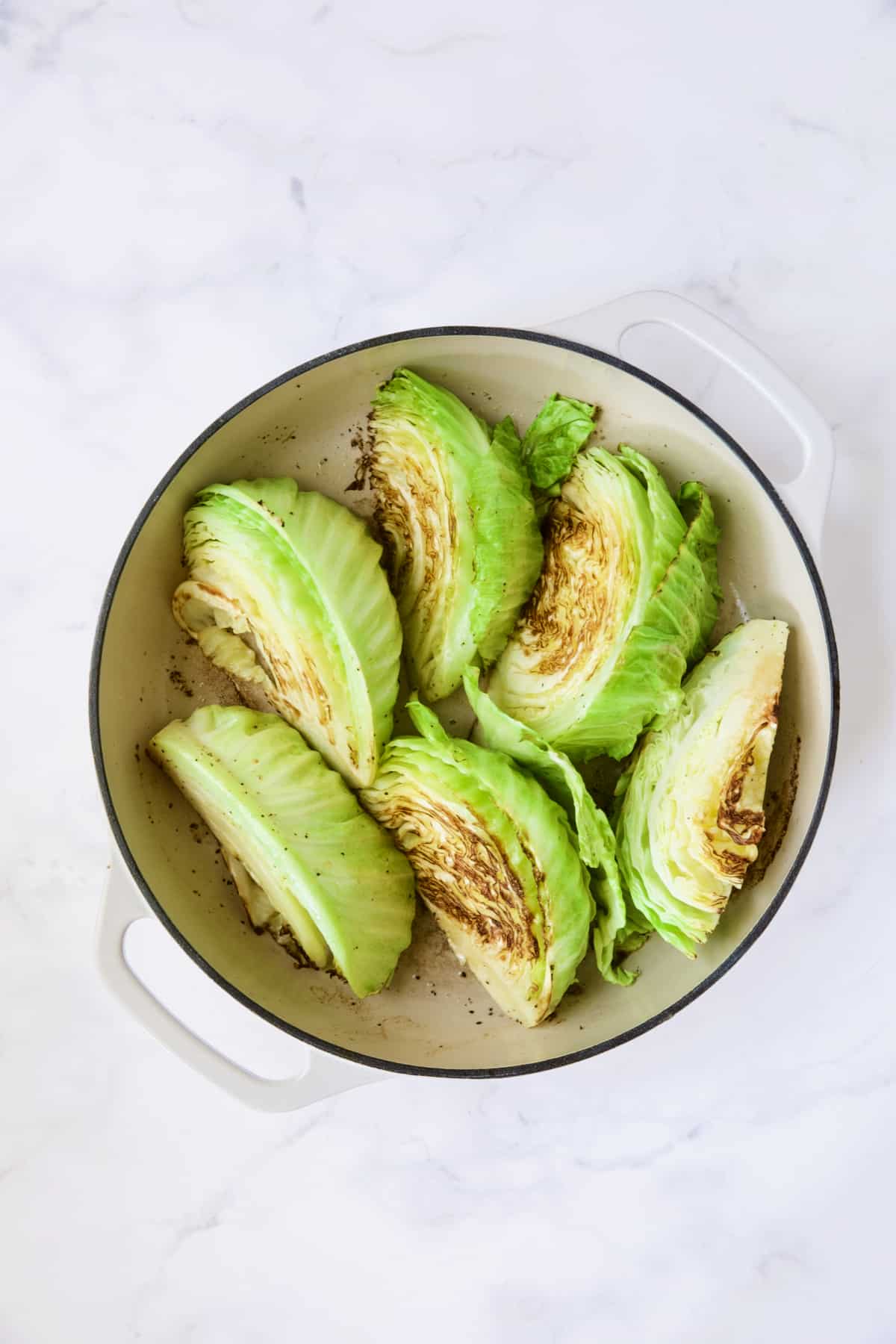 Six browned cabbage wedges in white enamel cast iron skillet.