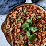 Cuban-Style Turkey Picadillo with Sweet Potatoes in white skillet with serving spoon garnished with fresh cilantro.
