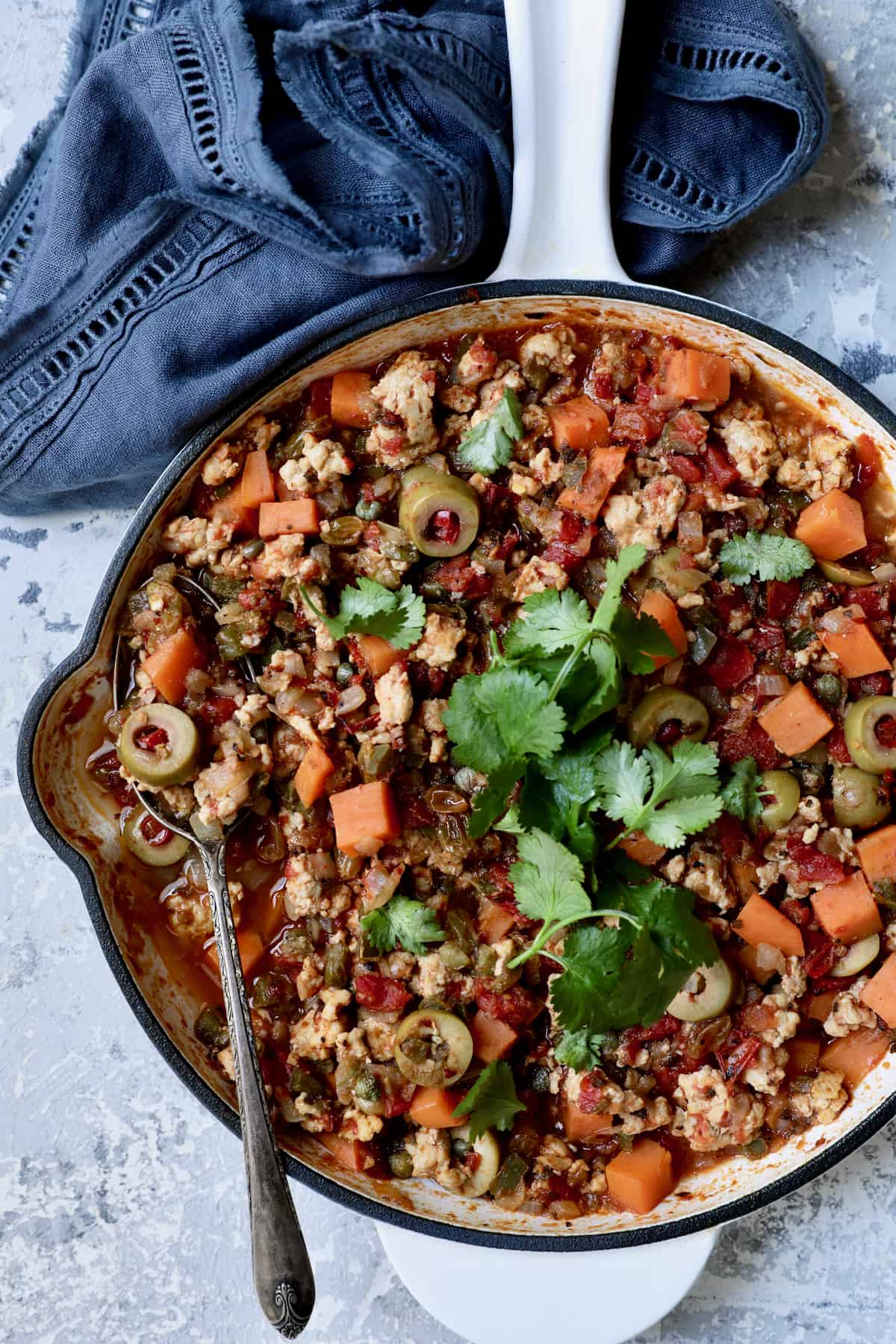 Cuban-Style Turkey Picadillo with Sweet Potatoes in white skillet with serving spoon garnished with fresh cilantro.