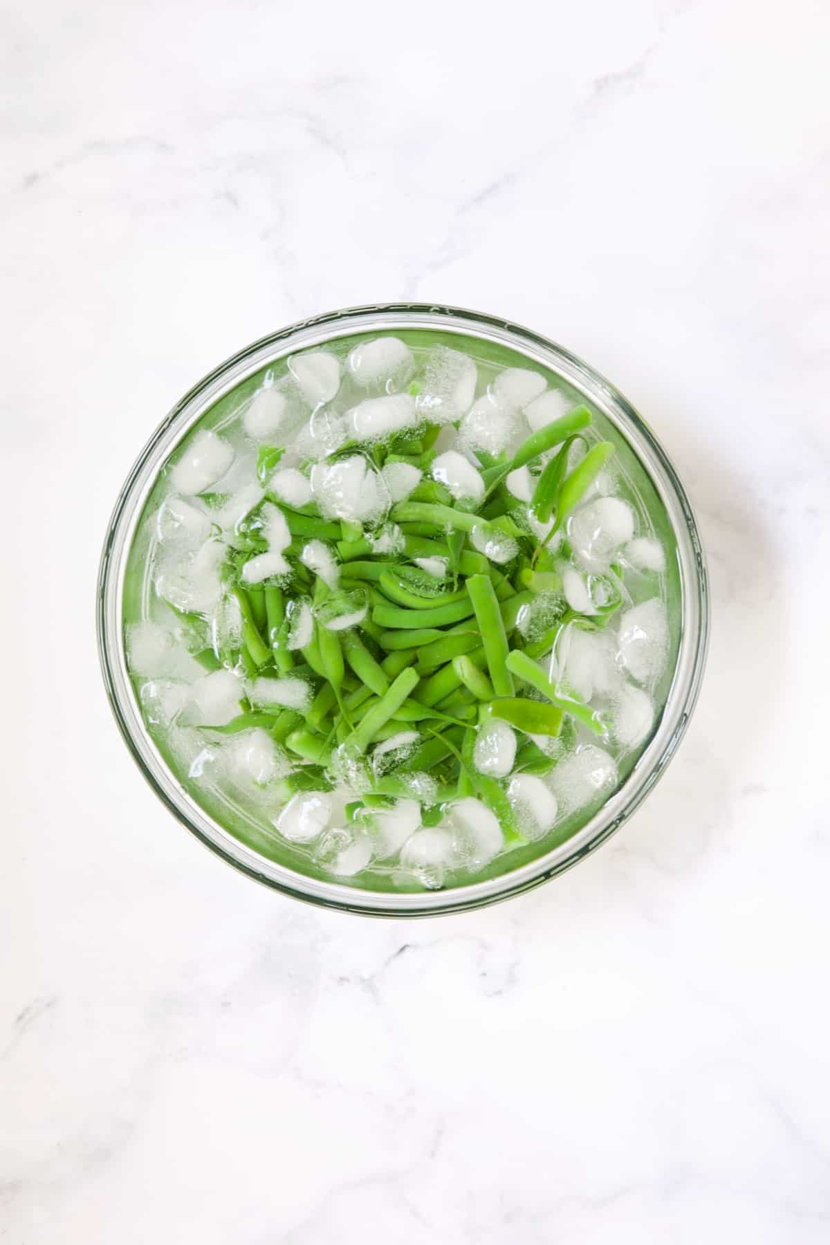 Green beans in ice water in glass bowl.