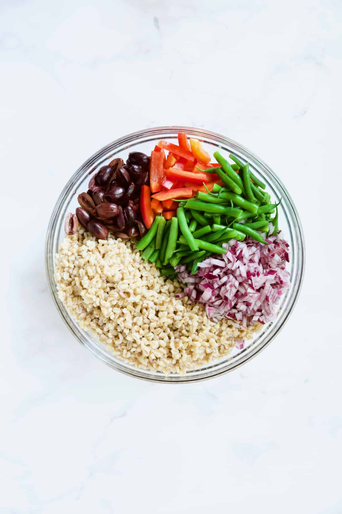 Ingredients for Mediterranean Barley Salad in glass bowl not yet stirred together.