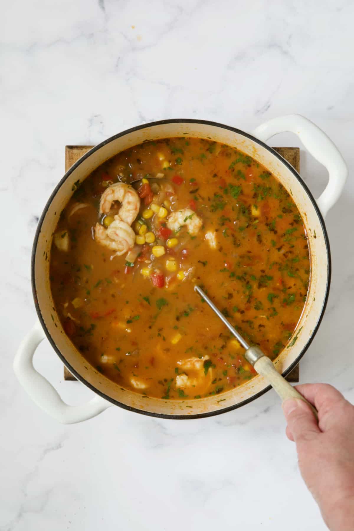 Shrimp and Corn Tortilla Soup in white Dutch oven being stirred with soup ladle.