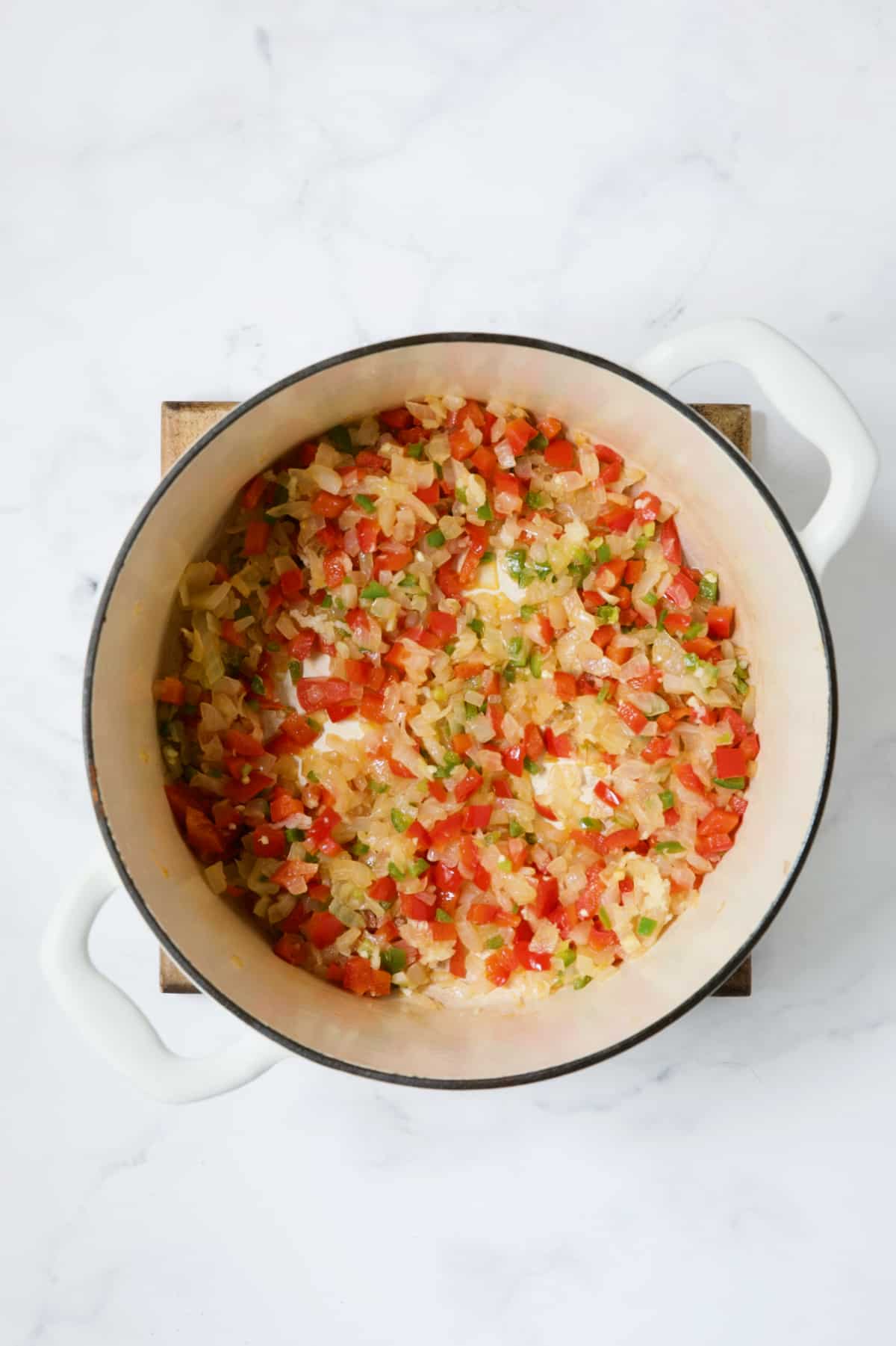 Cooked onion, red bel pepper and jalapeno in white Dutch oven.