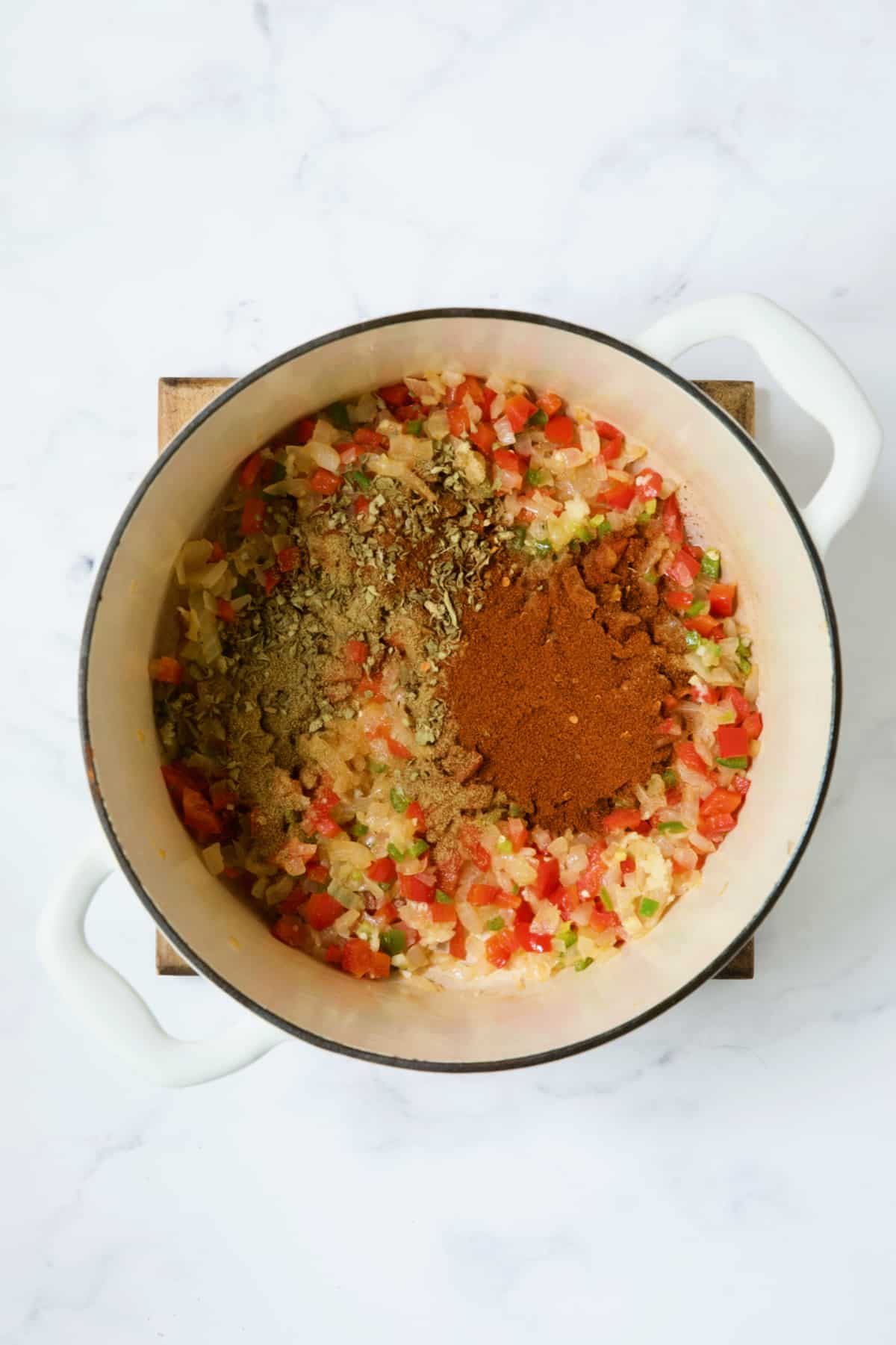Spices added to vegetables in white Dutch oven.