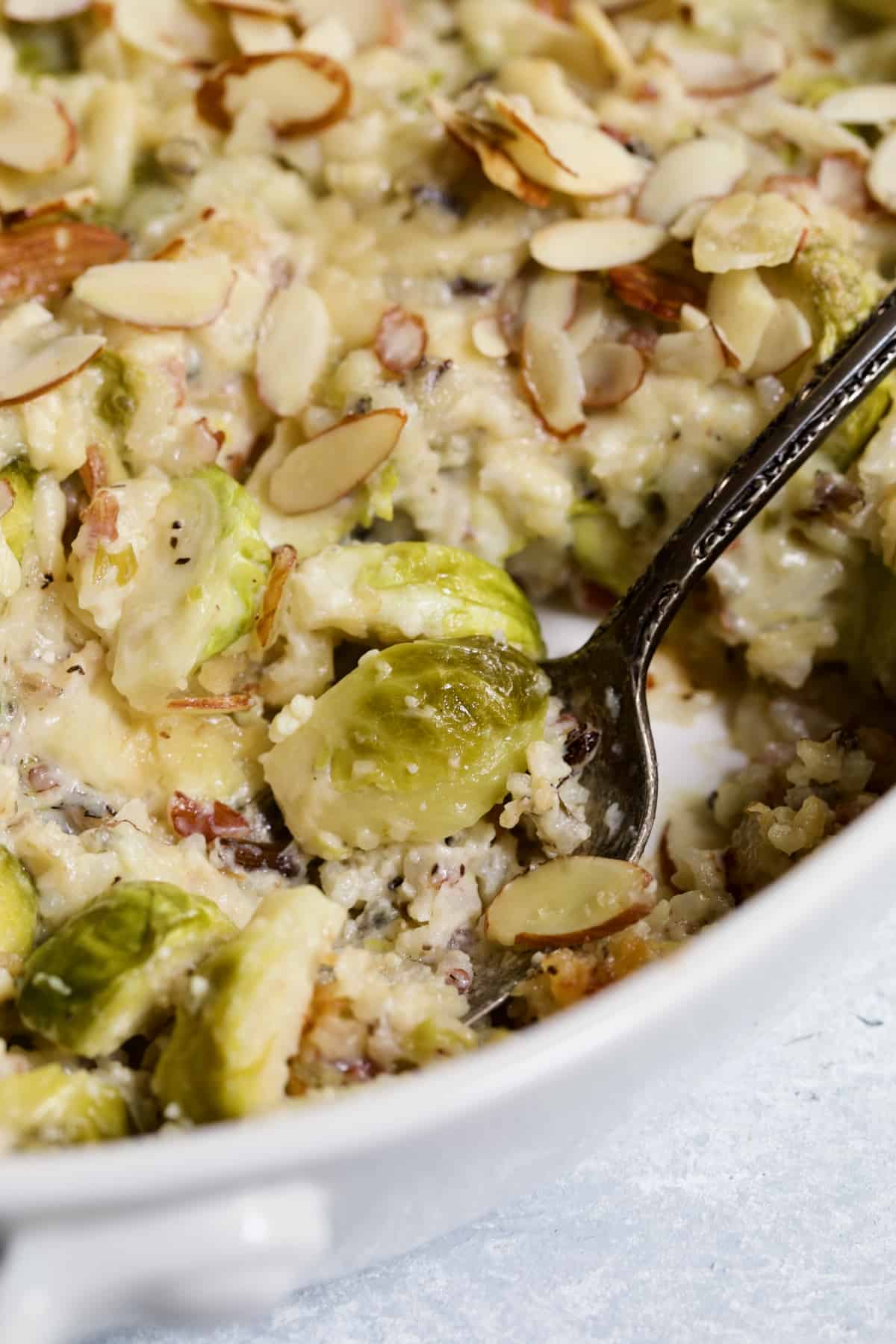 Brussels sprout and rice on serving spoon being scooped out of baking dish.