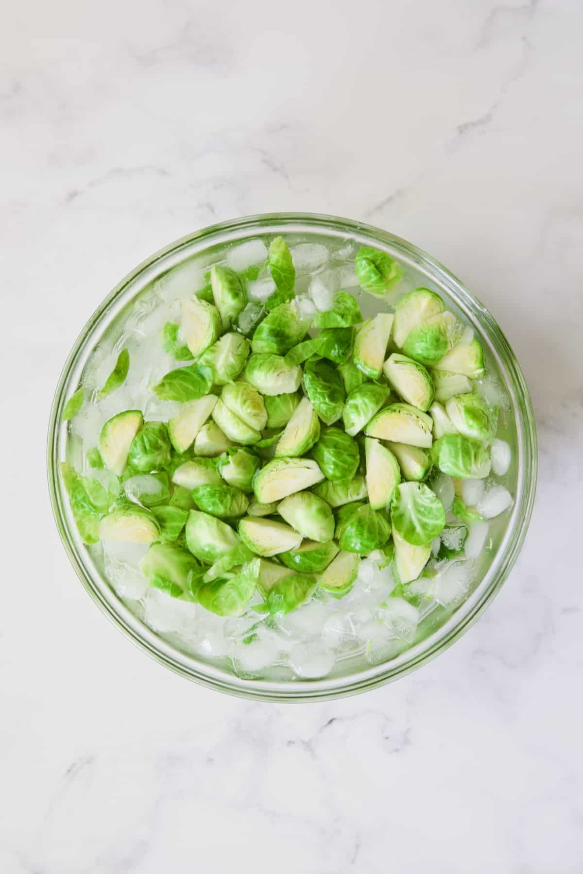 Quartered Brussels sprouts in ice water in glass bowl.