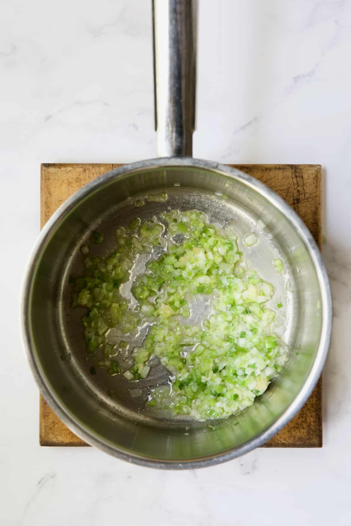 Scallions being cooked in butter in stainless steel saucepan.
