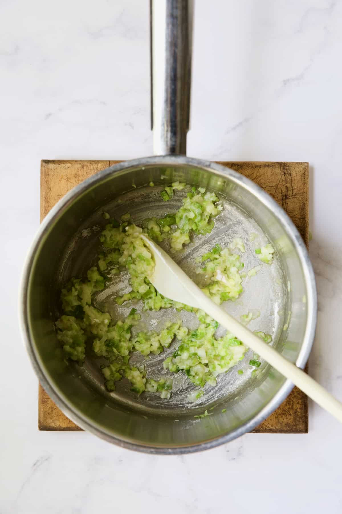 Scallions and flour being cooked in stainless steel saucepan.