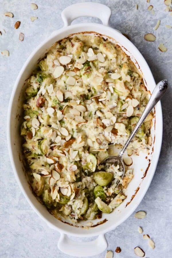 Cheesy Brussels Sprouts and Wild Rice Casserole in oval gratin dish with serving removed and serving spoon.