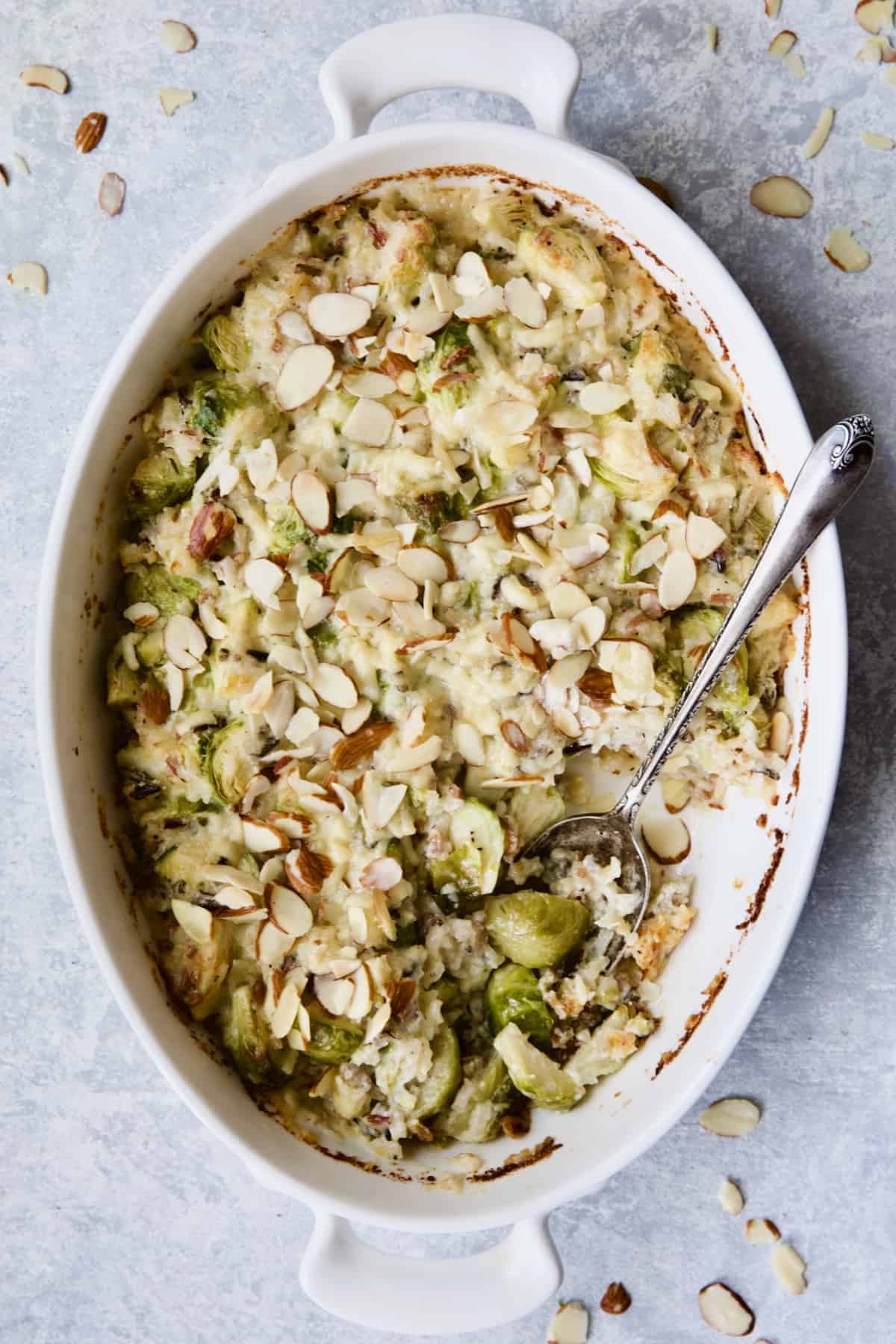 Cheesy Brussels Sprouts and Wild Rice Casserole in oval gratin dish with serving removed and serving spoon.