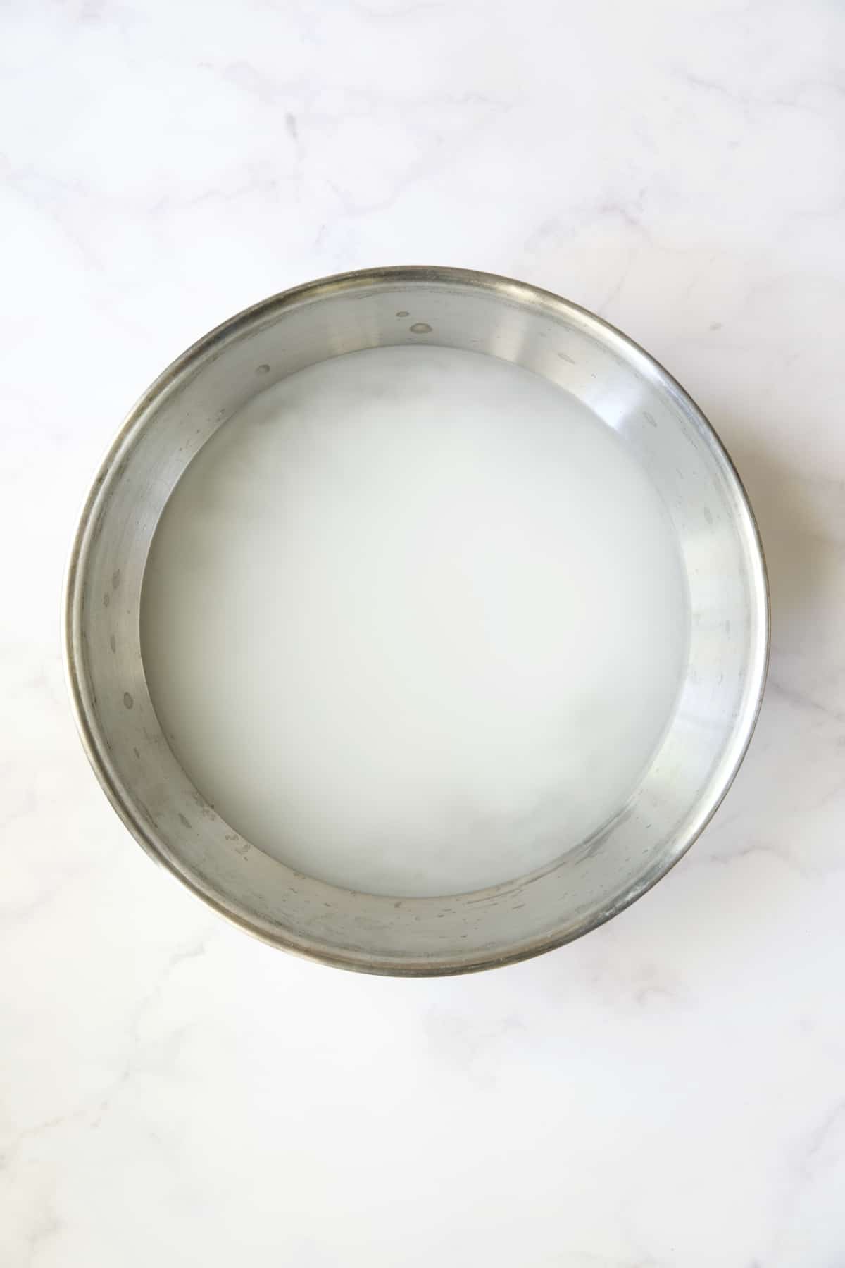 Sugar and salt added to hot water in stainless steel bowl.