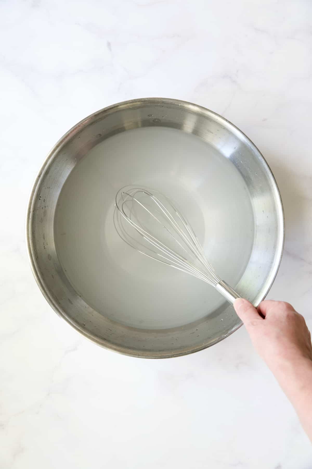 Hand whisking brine in stainless steel bowl.