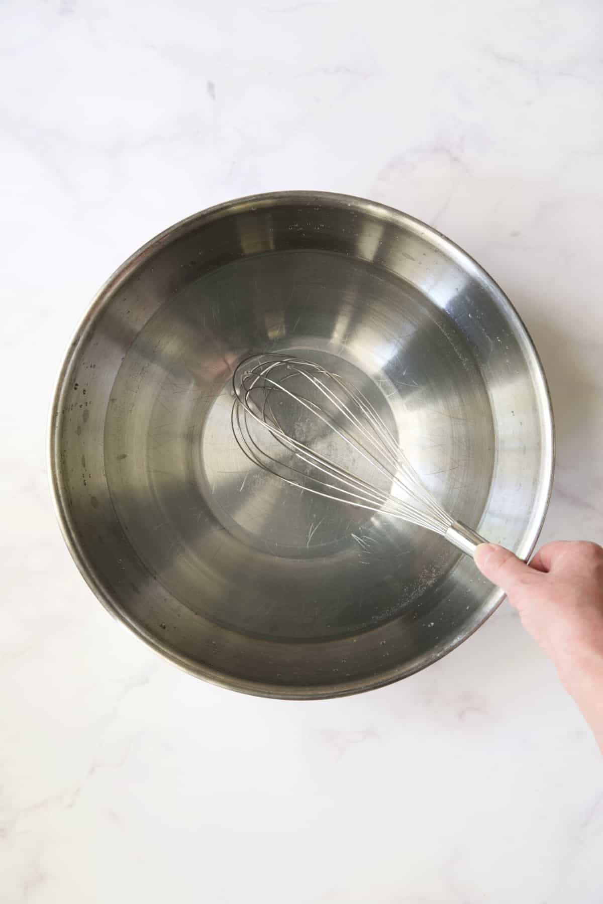 Hand whisking brine in stainless steel bowl.