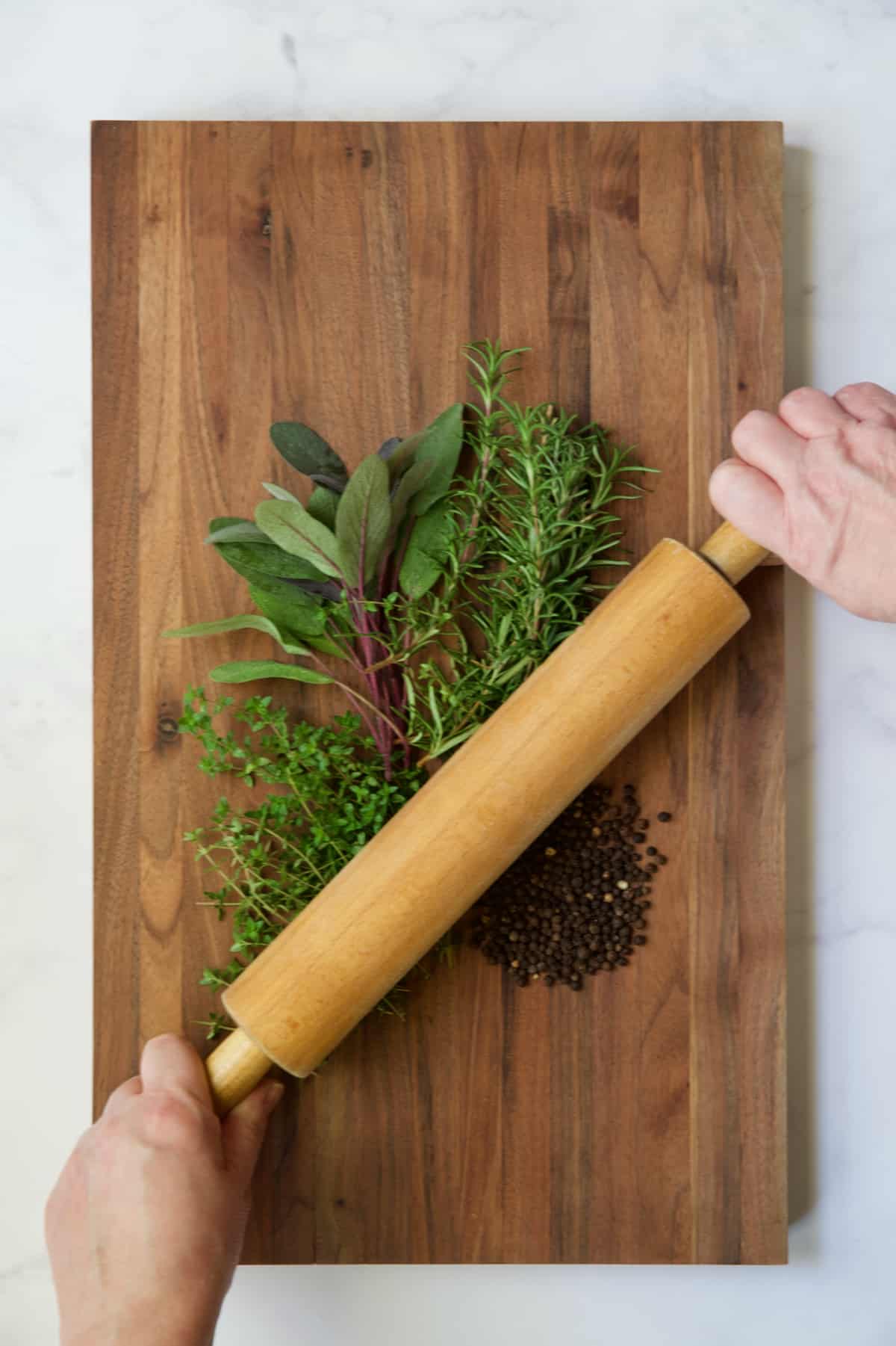 Herbs being crushed with rolling pin on wood cutting board.