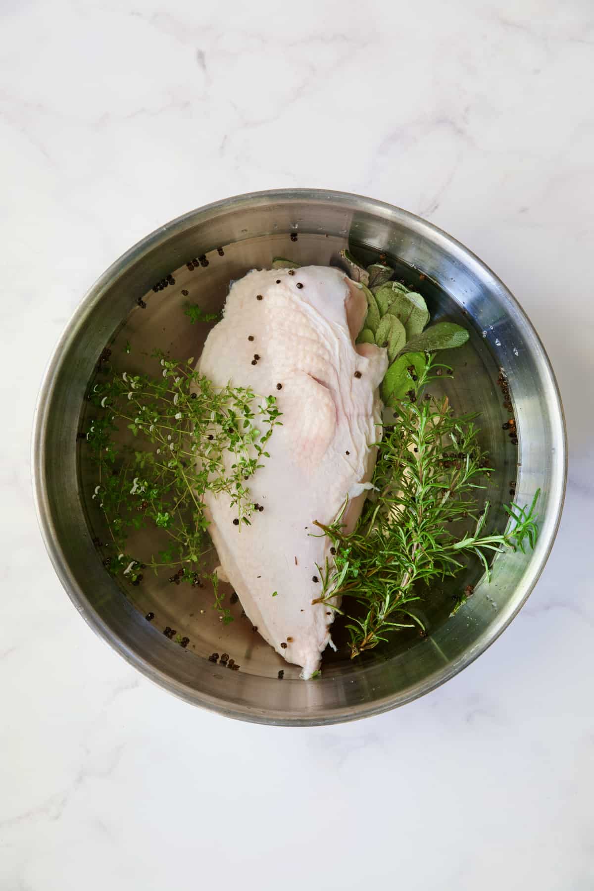 Turkey breast half in Easy Turkey Brine in stainless steel bowl.