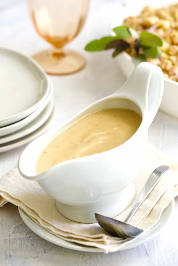 Gravy in white gravy boat on beige napkin with ladle.