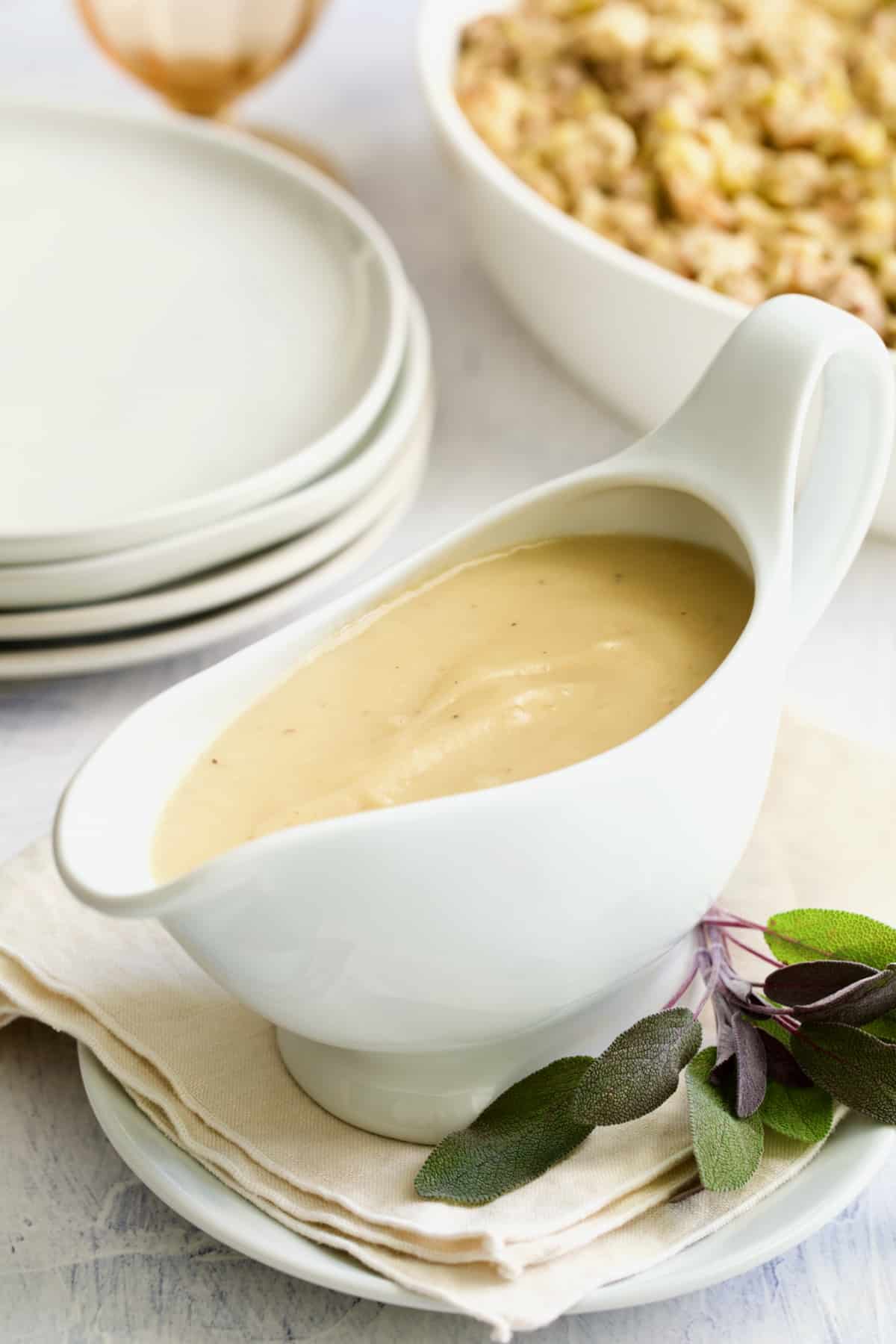 Gravy in white gravy boat on beige napkin with sage sprig.