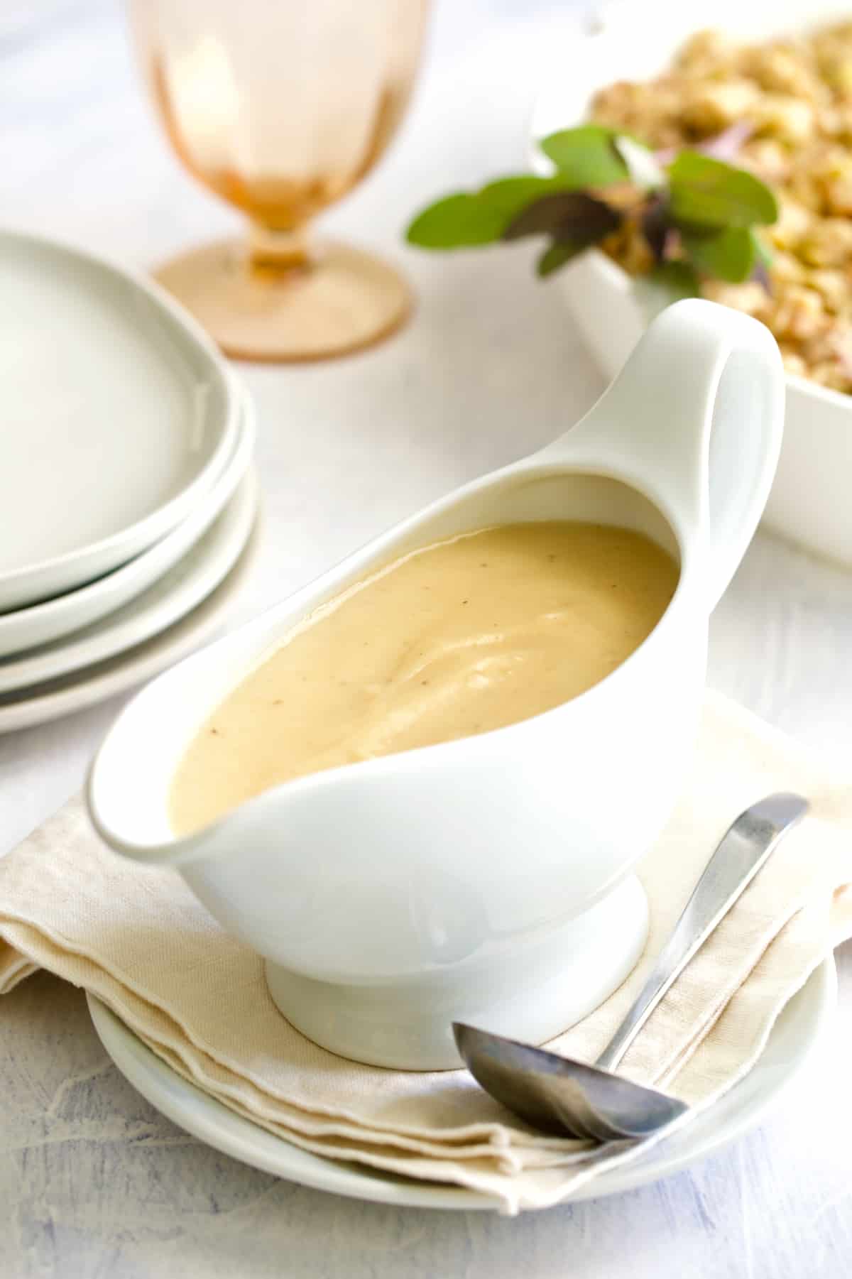 Gravy in white gravy boat on beige napkin with ladle.