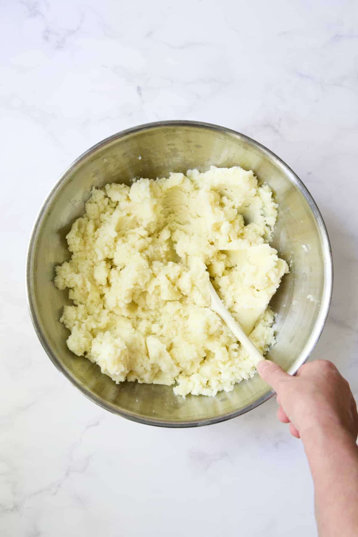 Potatoes being stirred in stainless steel bowl.