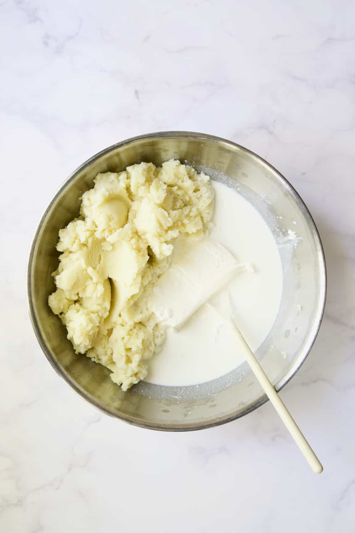 Potatoes with cream cheese, sour cream and half-and-half in stainless steel bowl.