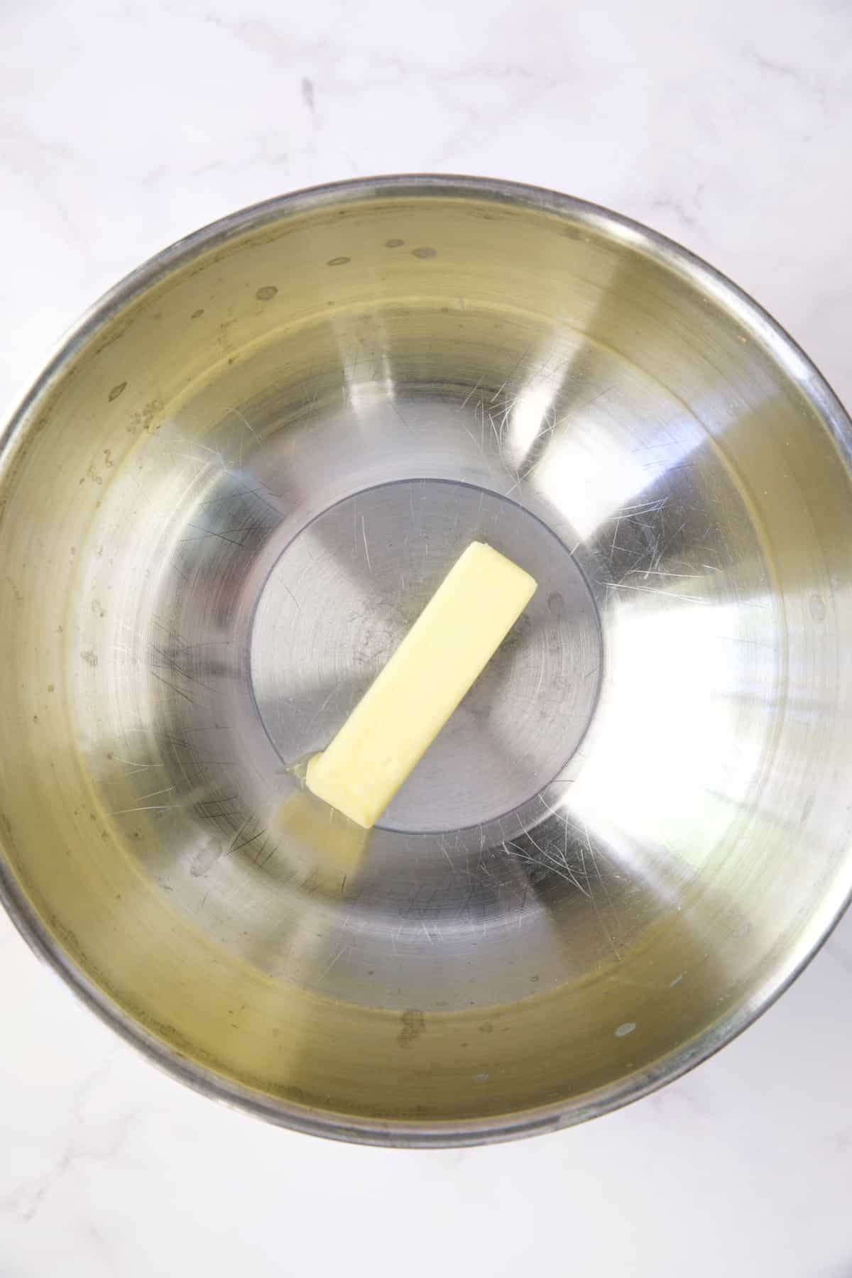 Stick of butter in stainless steel bowl.