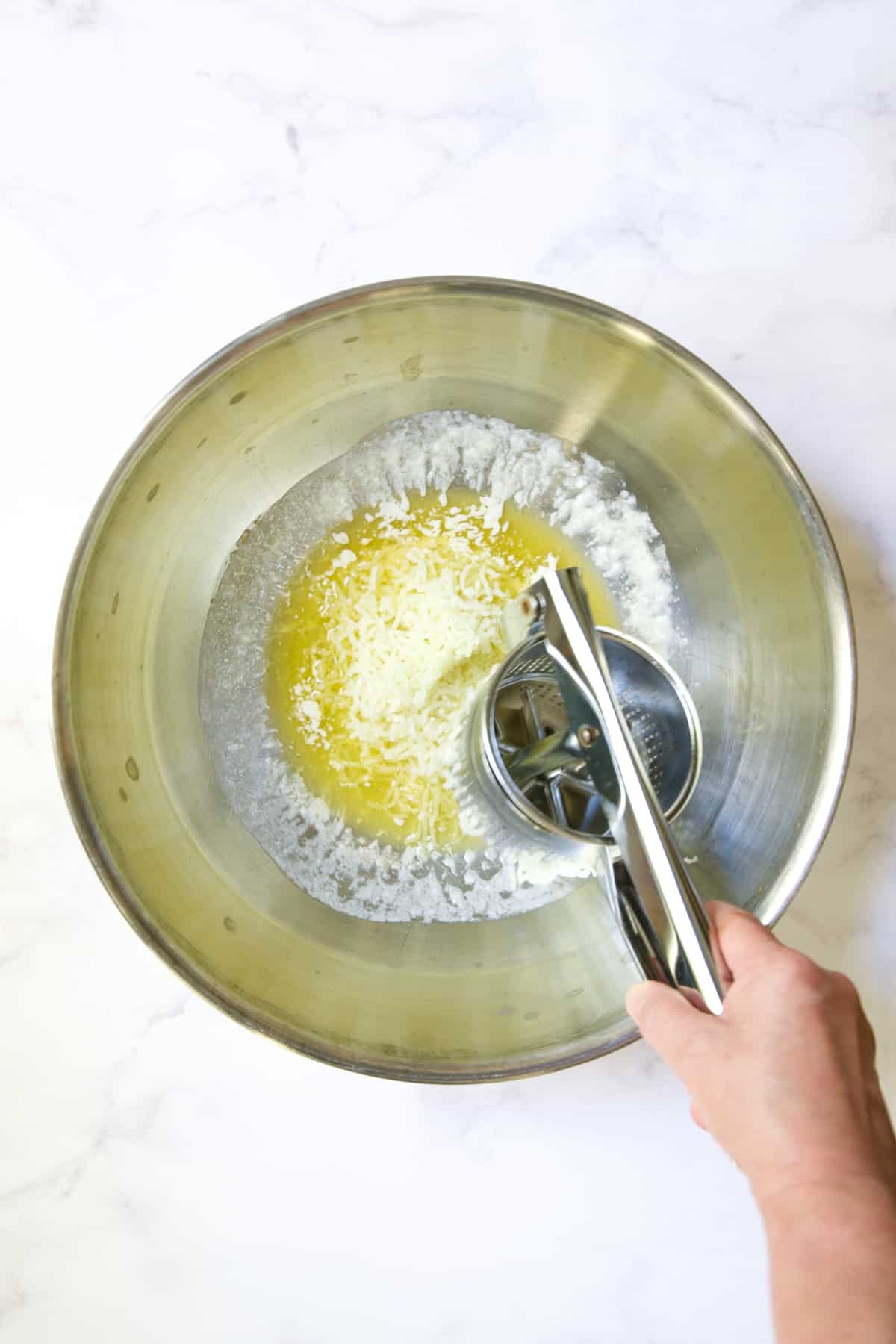 Potatoes being riced into melted butter in stainless steel bowl.