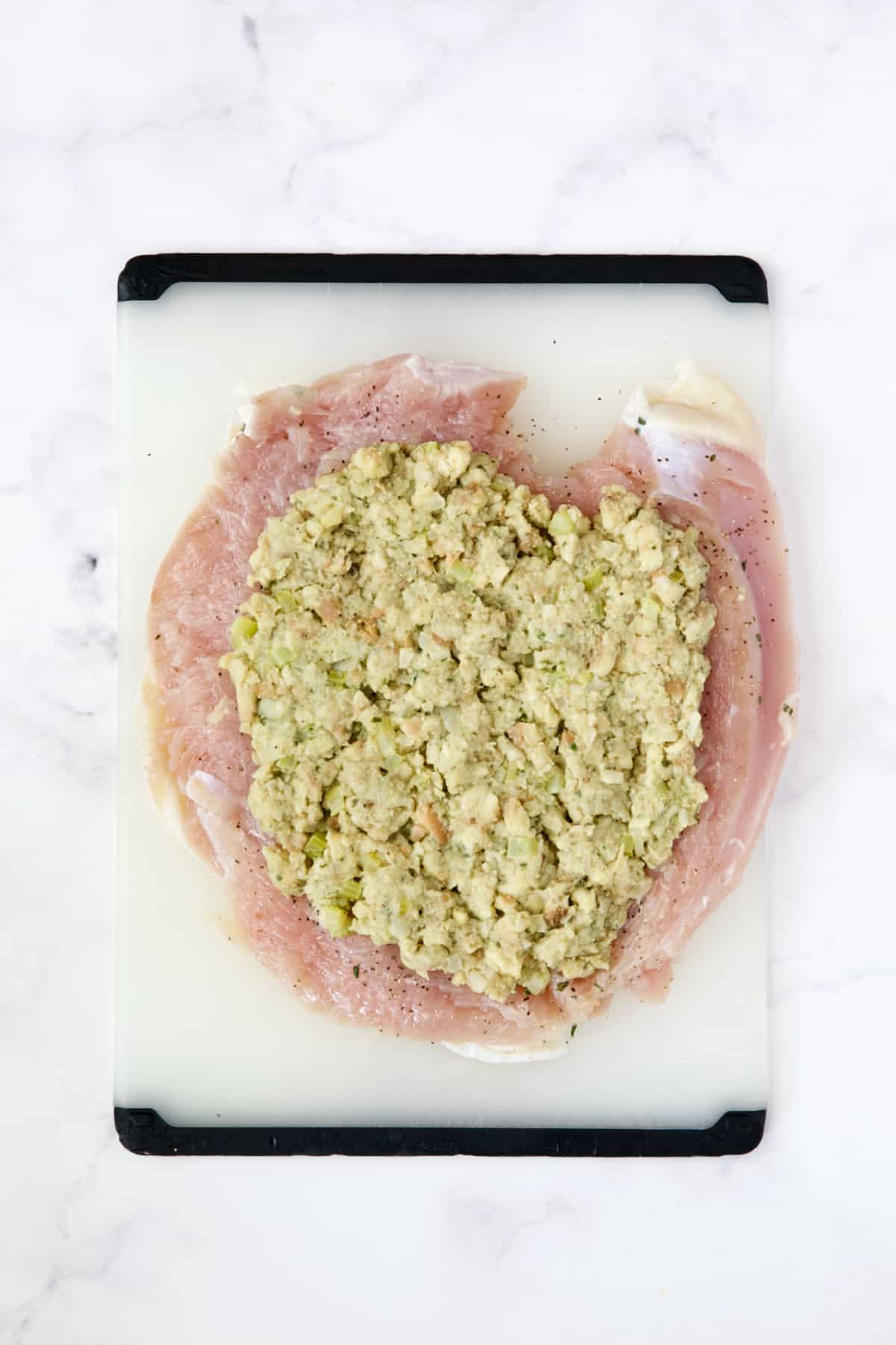 Uncooked flattened turkey breast with stuffing spread on the inside.