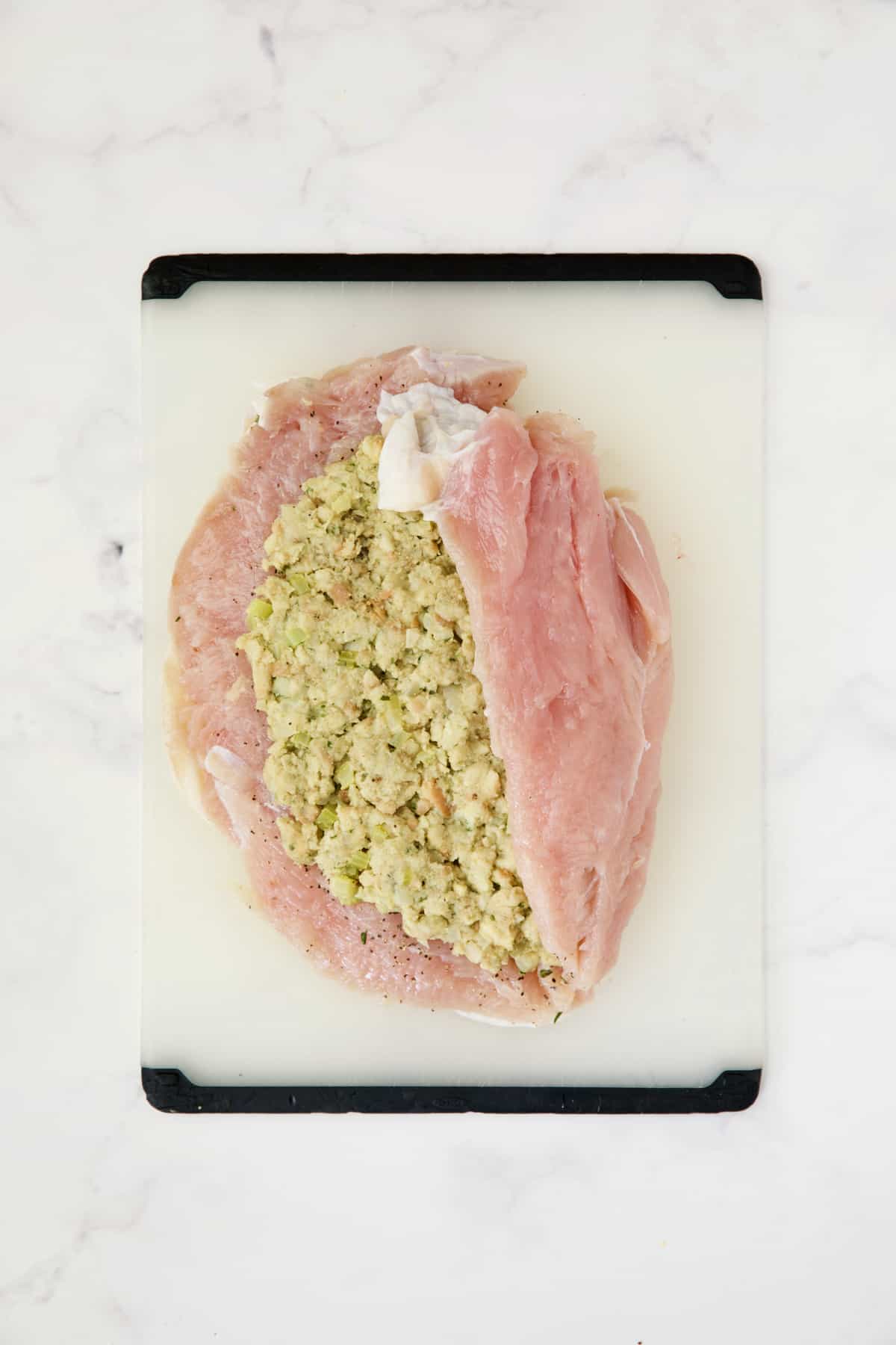 Uncooked turkey breast with stuffing and right side folded over.