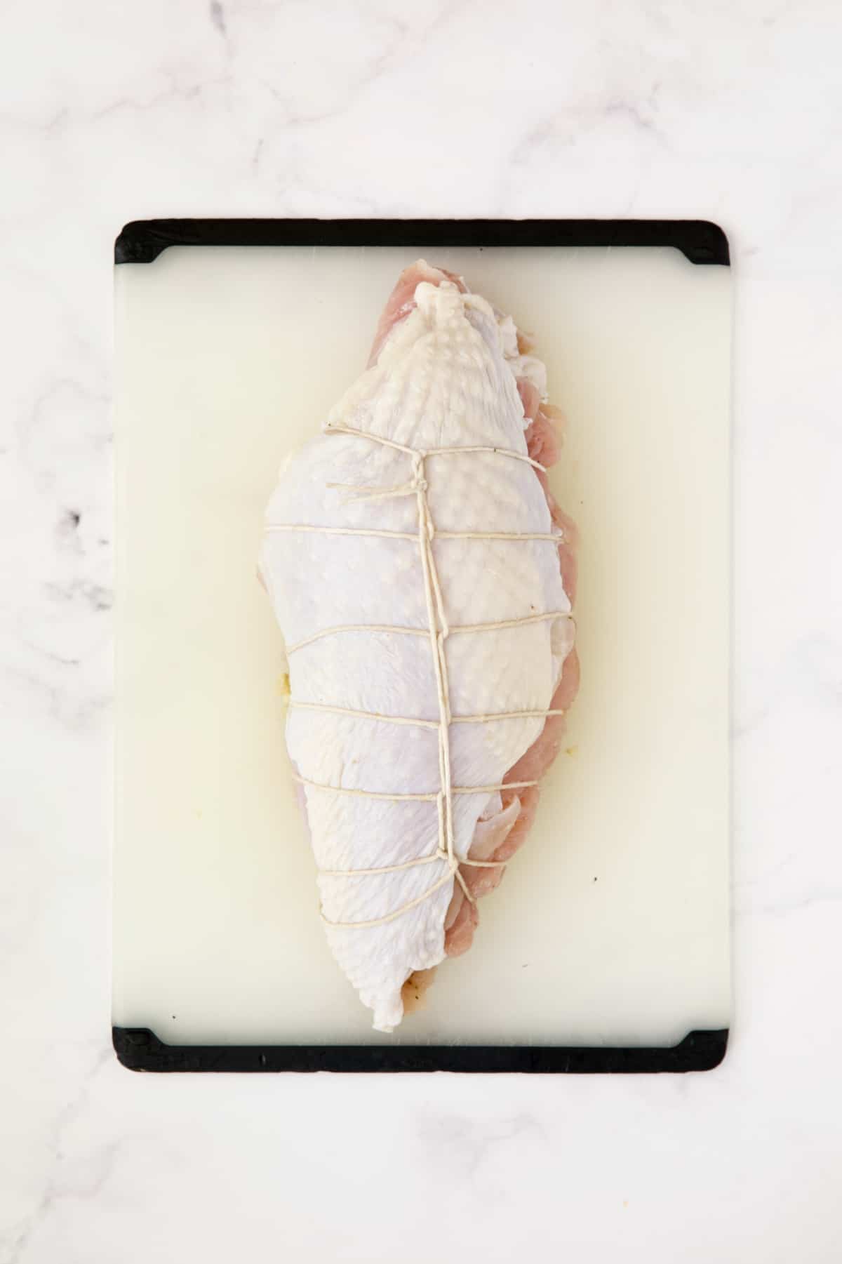 Uncooked stuffed turkey breast on white plastic cutting board.