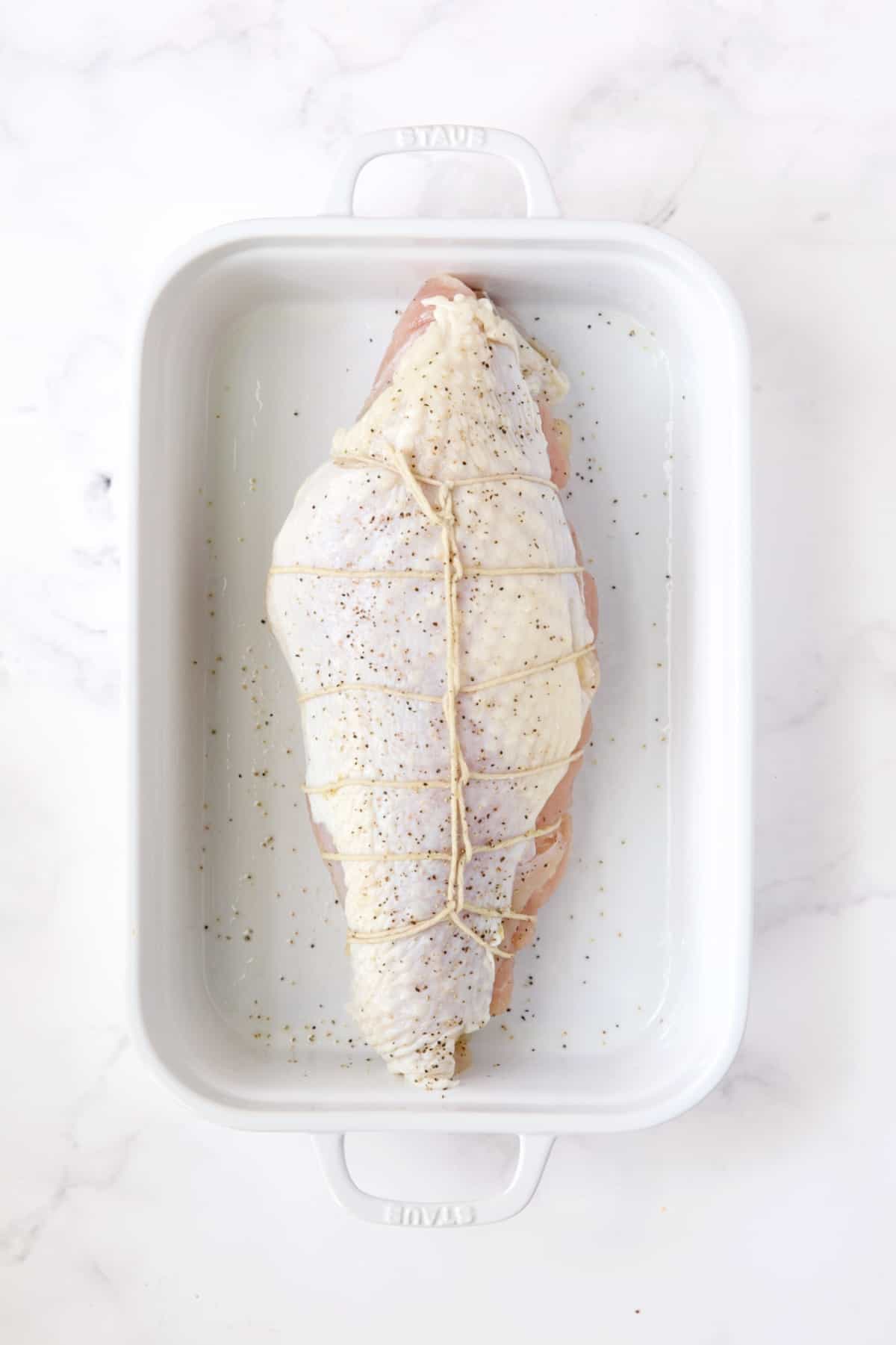 Uncooked stuffed turkey breast in white roasting pan.