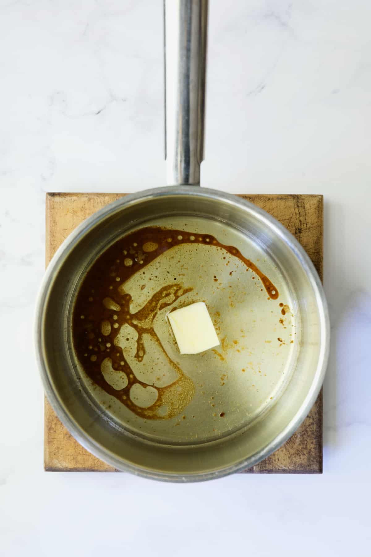Square of butter added to turkey drippings in stainless steel saucepan.