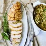 Roast Turkey Breast with Traditional Stuffing on white platter garnished with fresh herbs.