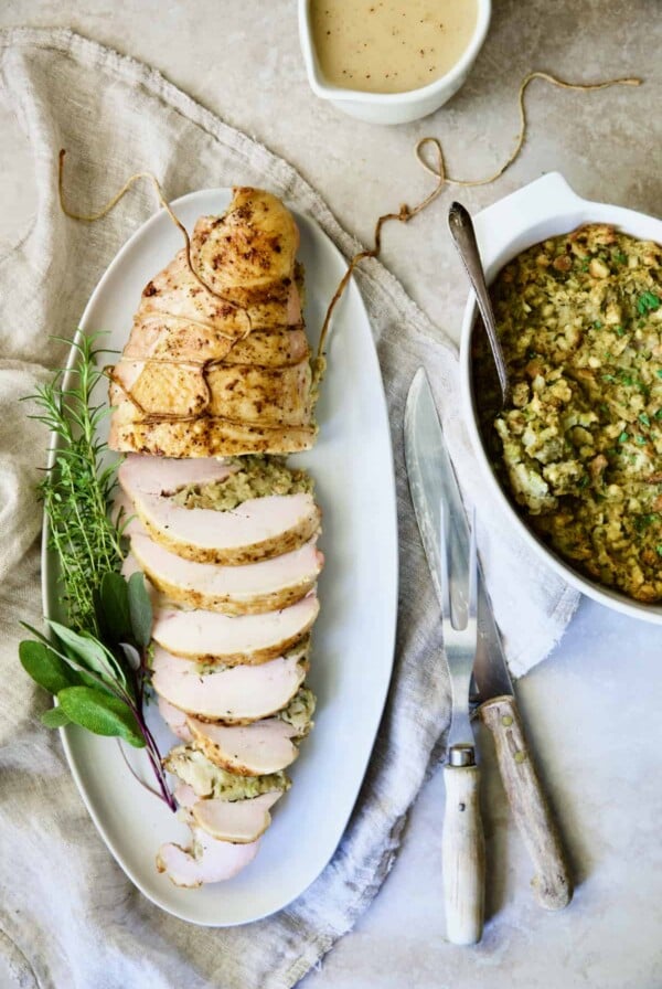 Roast Turkey Breast with Traditional Stuffing on white platter garnished with fresh herbs.