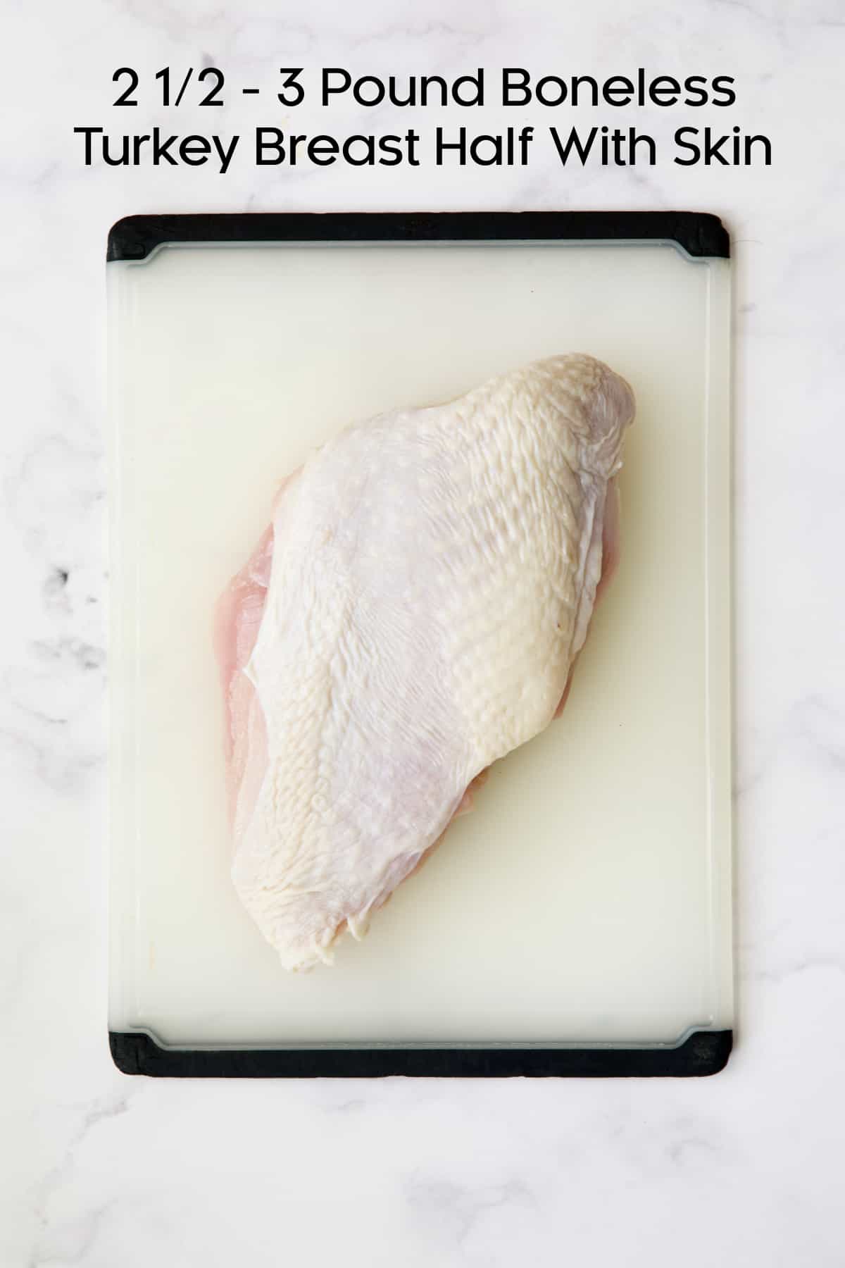 Boneless turkey breast half with skin on white plastic cutting board.