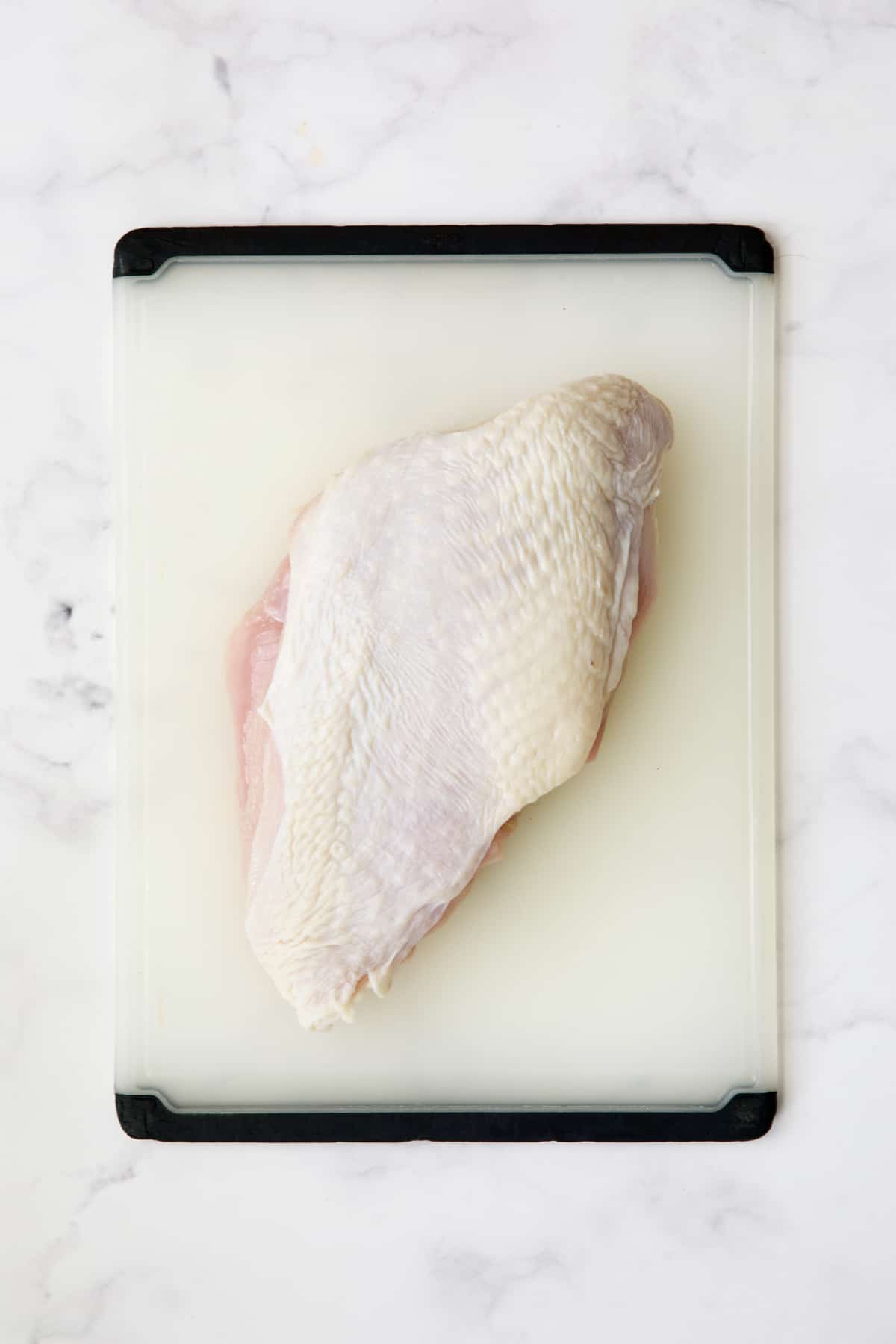 Boneless turkey breast half with skin on white plastic cutting board.