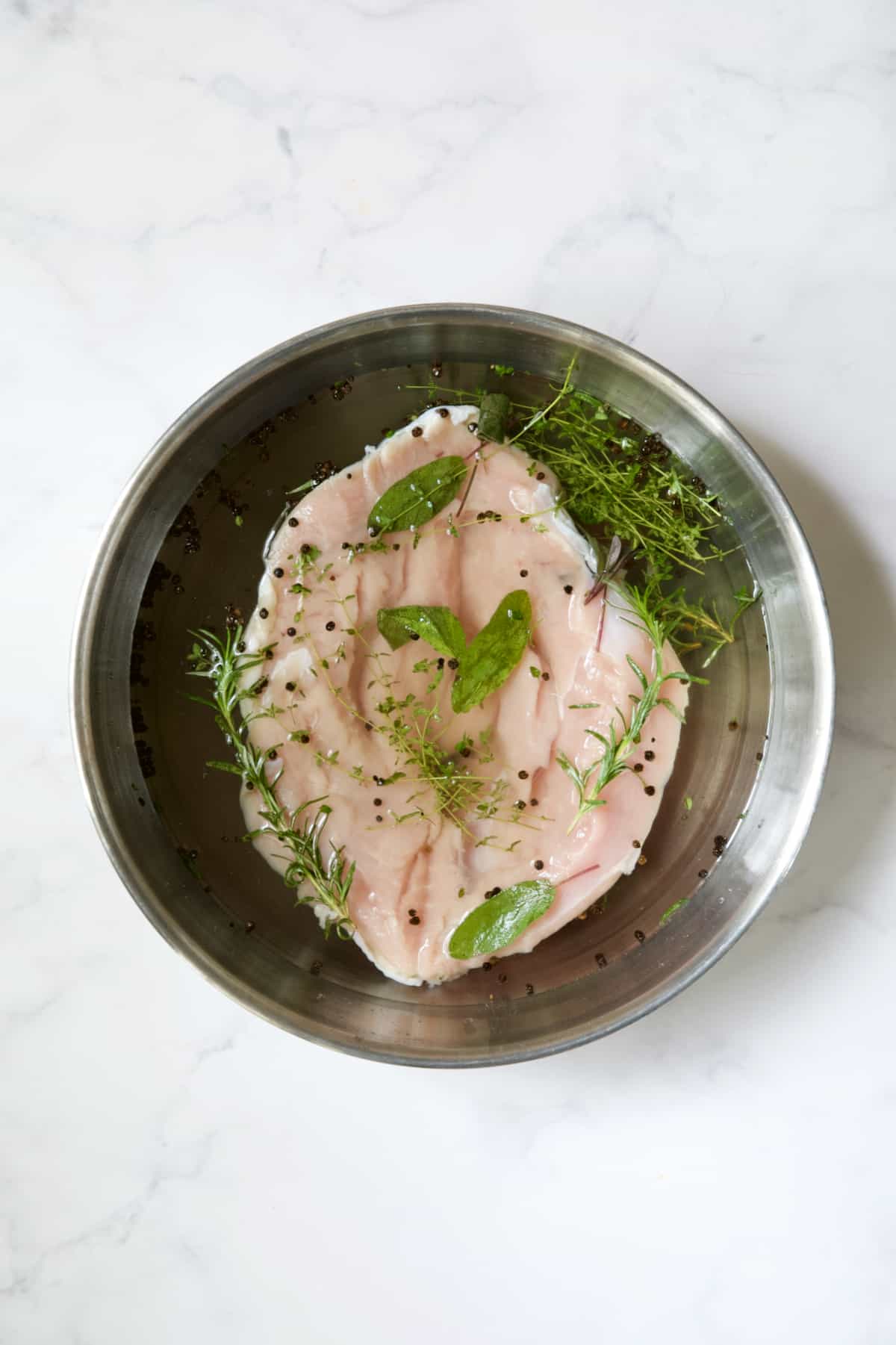 Butterflied turkey breast in brine in stainless steel bowl.