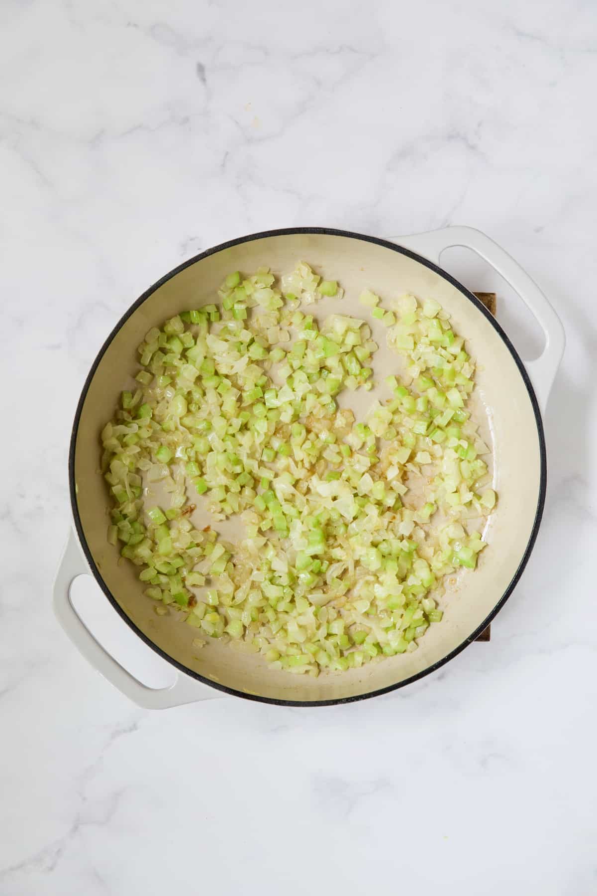 Cooked onions and celery in white enamel cast iron skillet.