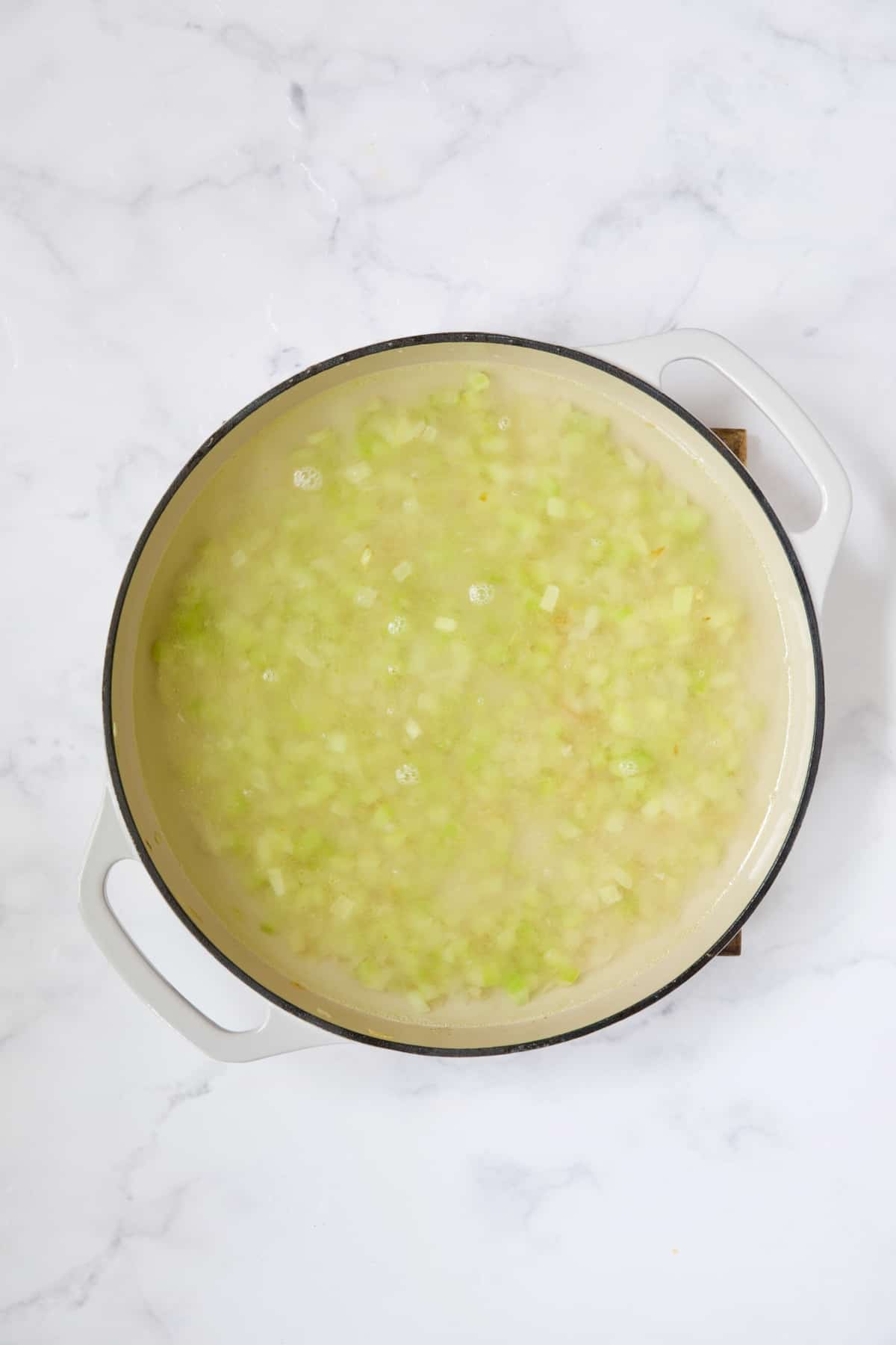 Onions, celery and broth in white enamel cast iron skillet.