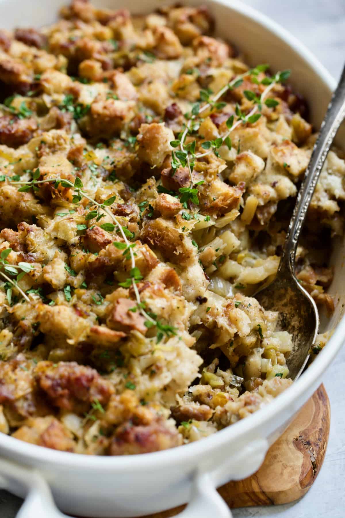 Sausage Stuffing with Fennel and Leeks in white oval gratin dish with serving spoon.