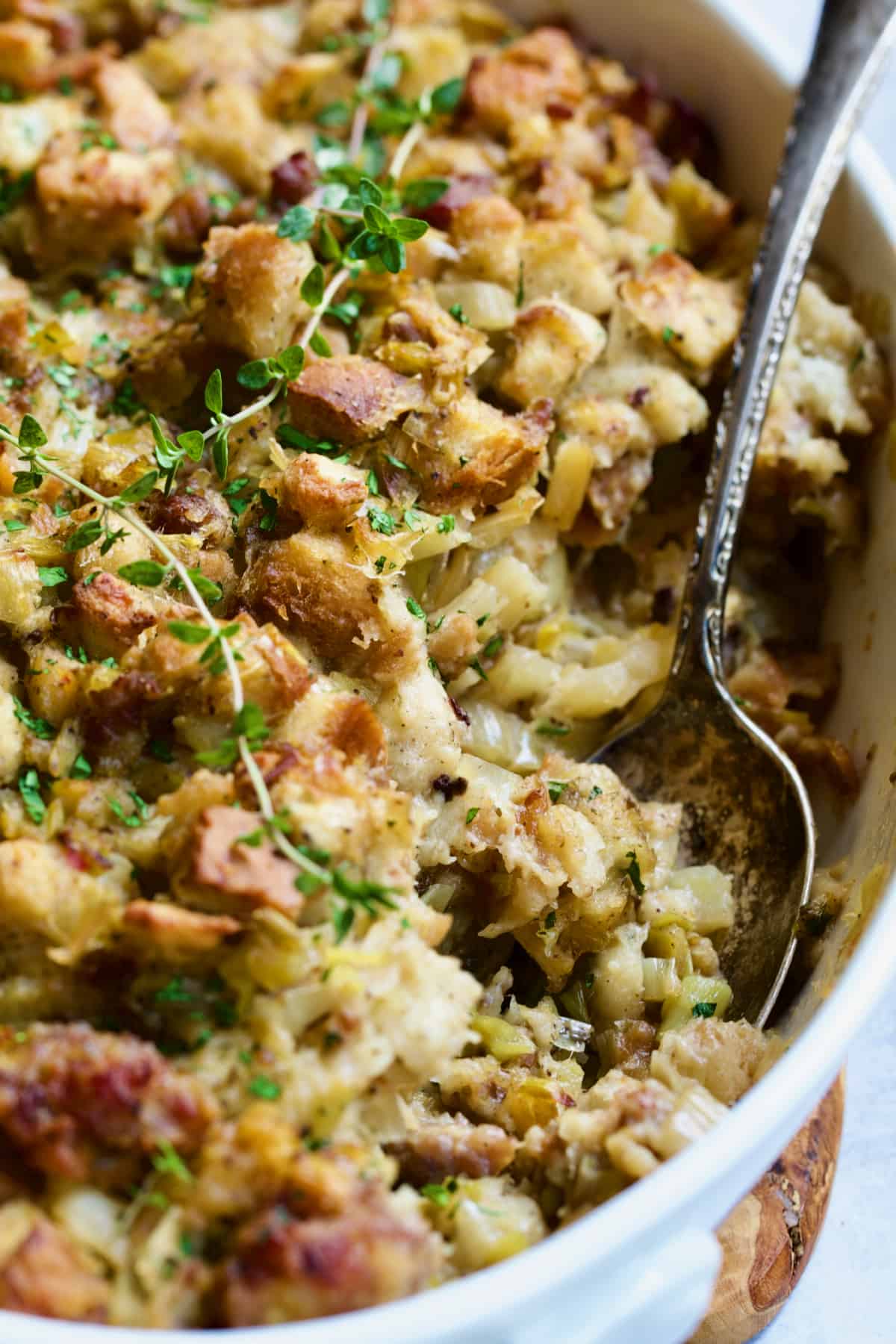 Sausage Stuffing with Fennel and Leeks in white oval gratin dish with serving spoon.