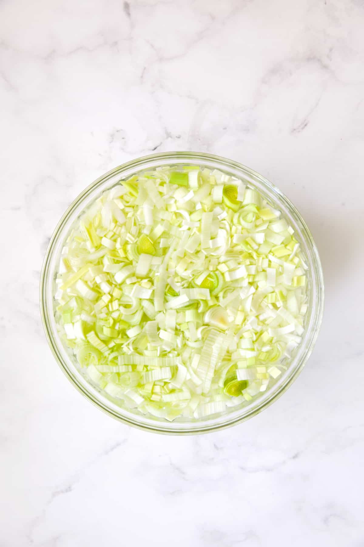Leeks in water in glass bowl.