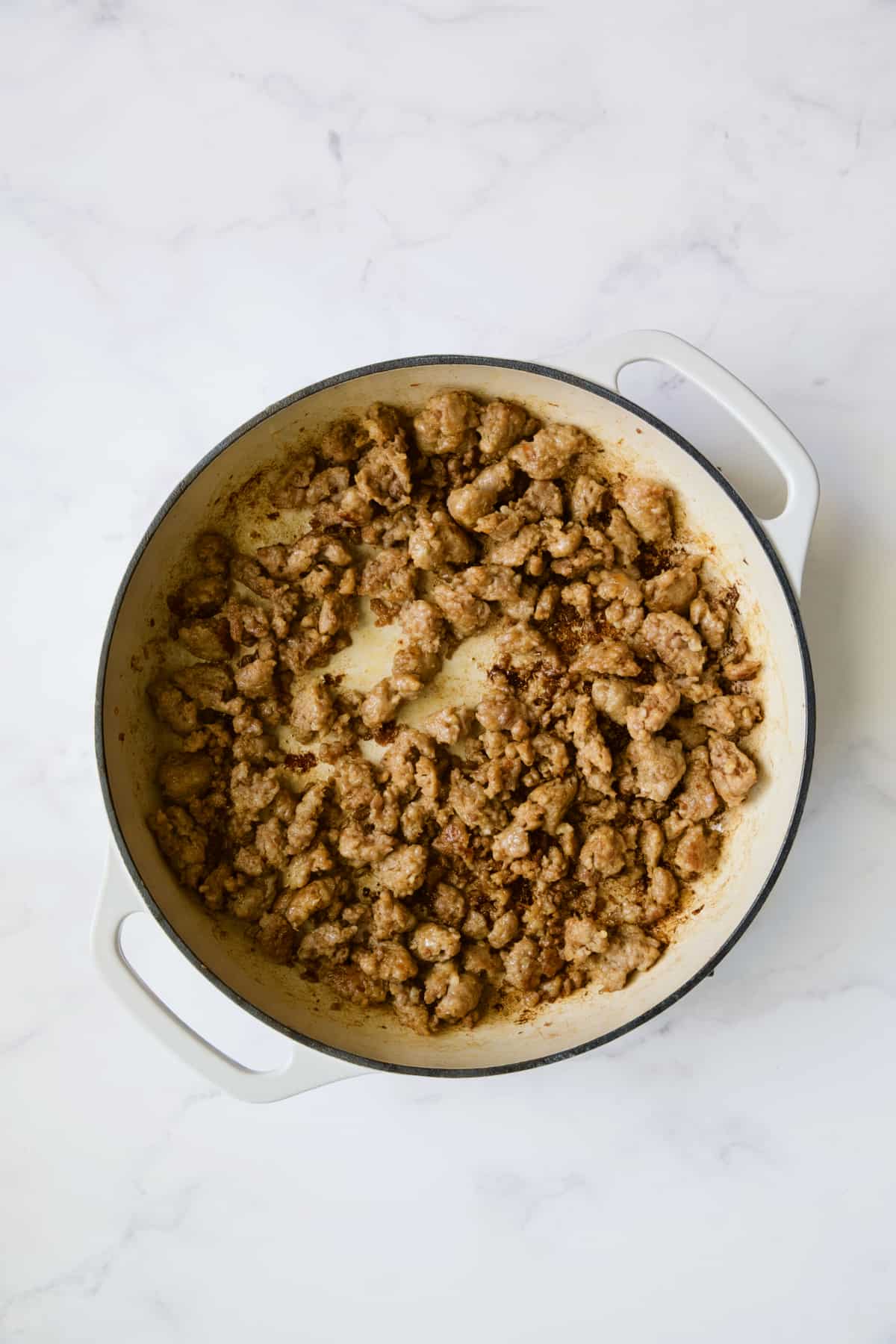 Cooked Italian sausage in white enamel cast iron skillet.