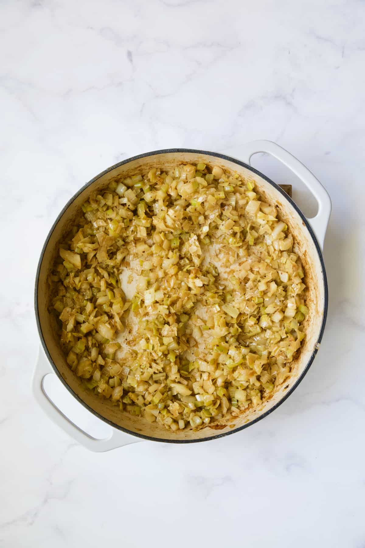 Cooked fennel, leeks and celery in white enamel cast iron skillet.