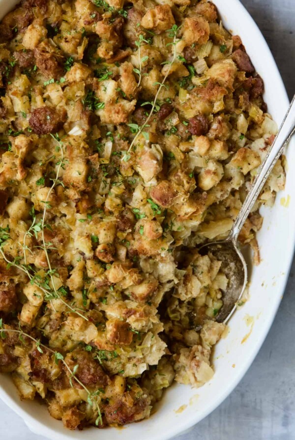Sausage Stuffing with Fennel and Leeks in white oval gratin dish with serving spoon.