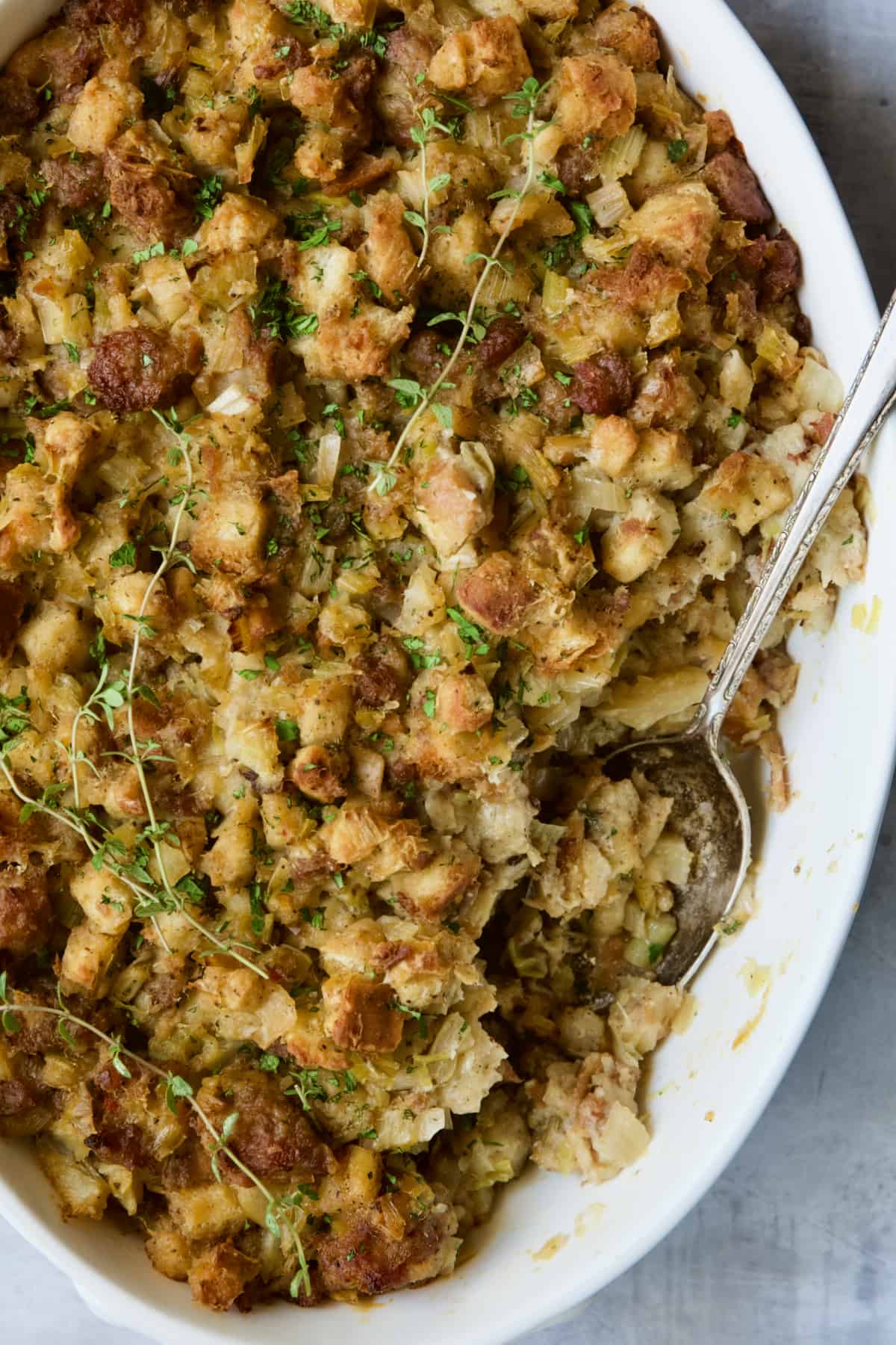 Sausage Stuffing with Fennel and Leeks in white oval gratin dish with serving spoon.