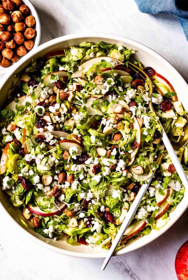 Shaved Brussels Sprouts Salad in white bowl with serving utensils.