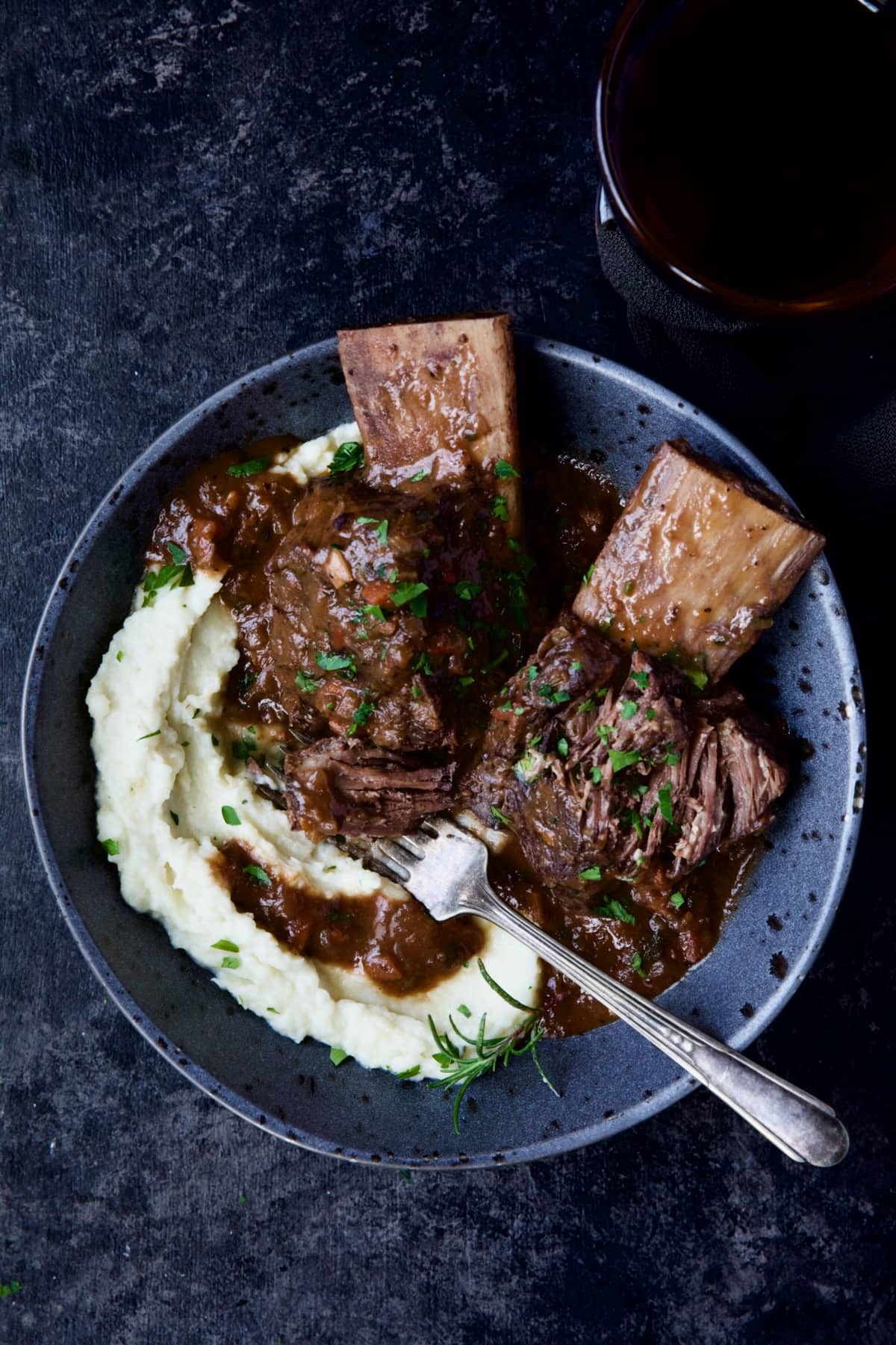 One bowl of Braised Beef Short Ribs with Cauliflower Leek Puree with wine glass.